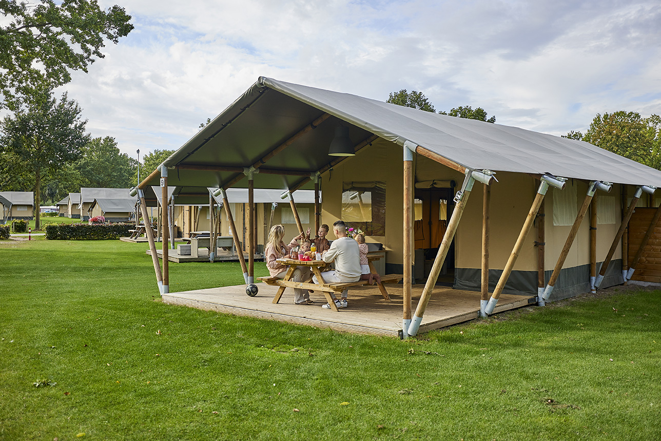 Een luxe safaritent met een houten veranda en een picknicktafel op een ruim grasveld op Recreatiepark De Leistert.