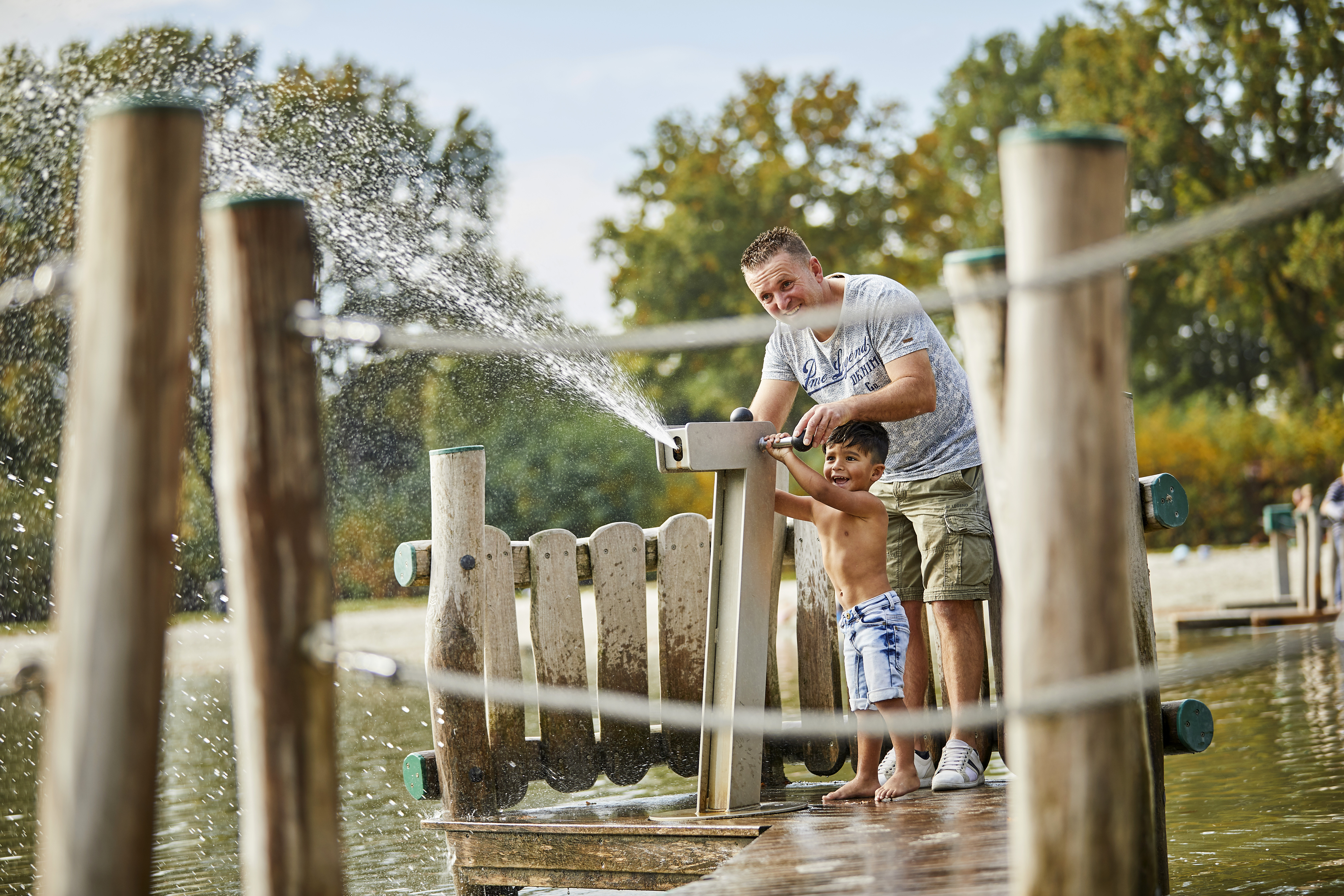 Een vader en zoon spelen samen met een groot waterkanon op een houten vlonder bij de recreatieplas van De Leistert.