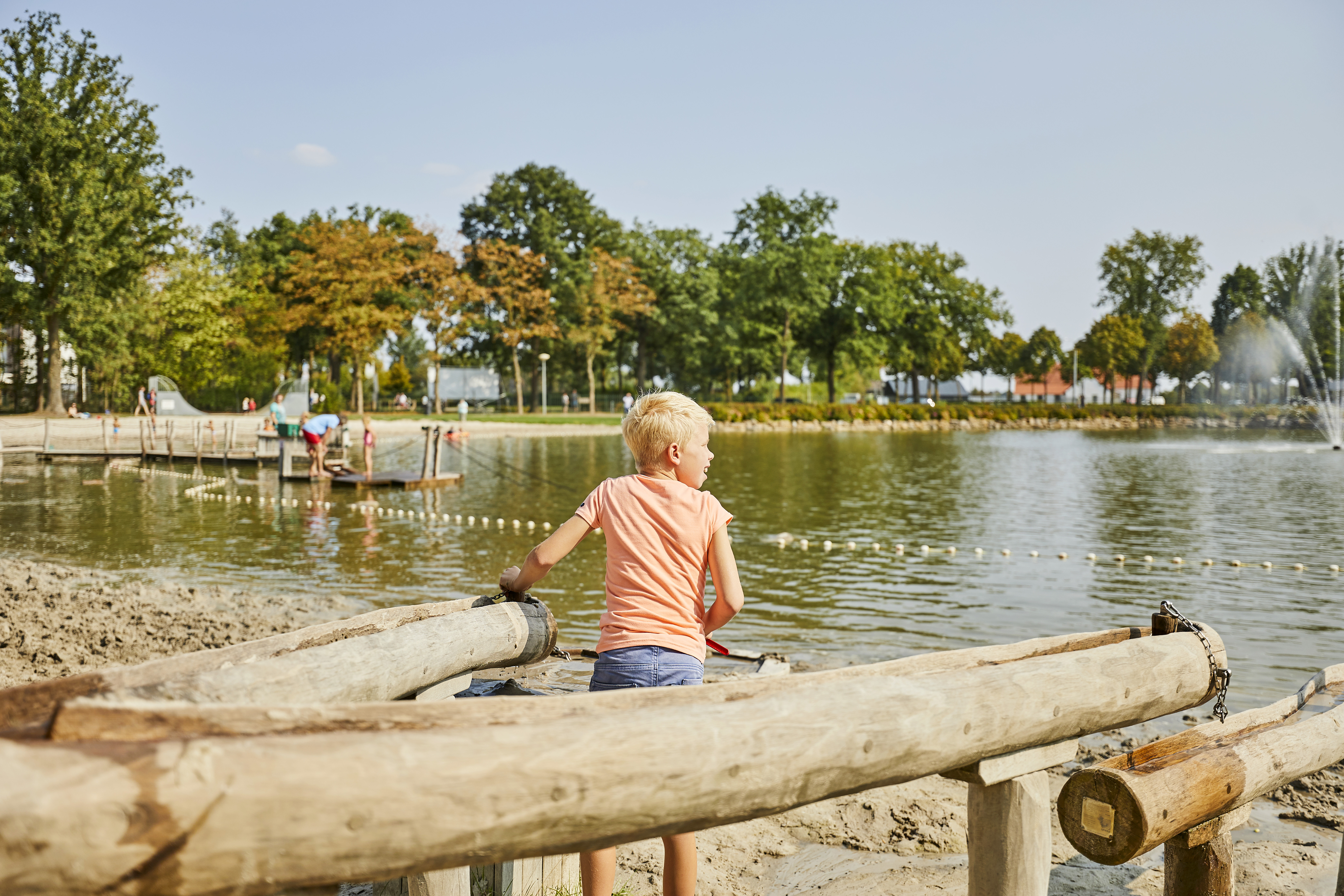 Een kind speelt met houten watergoten aan de rand van de recreatieplas op het dagstrand van Recreatiepark De Leistert.