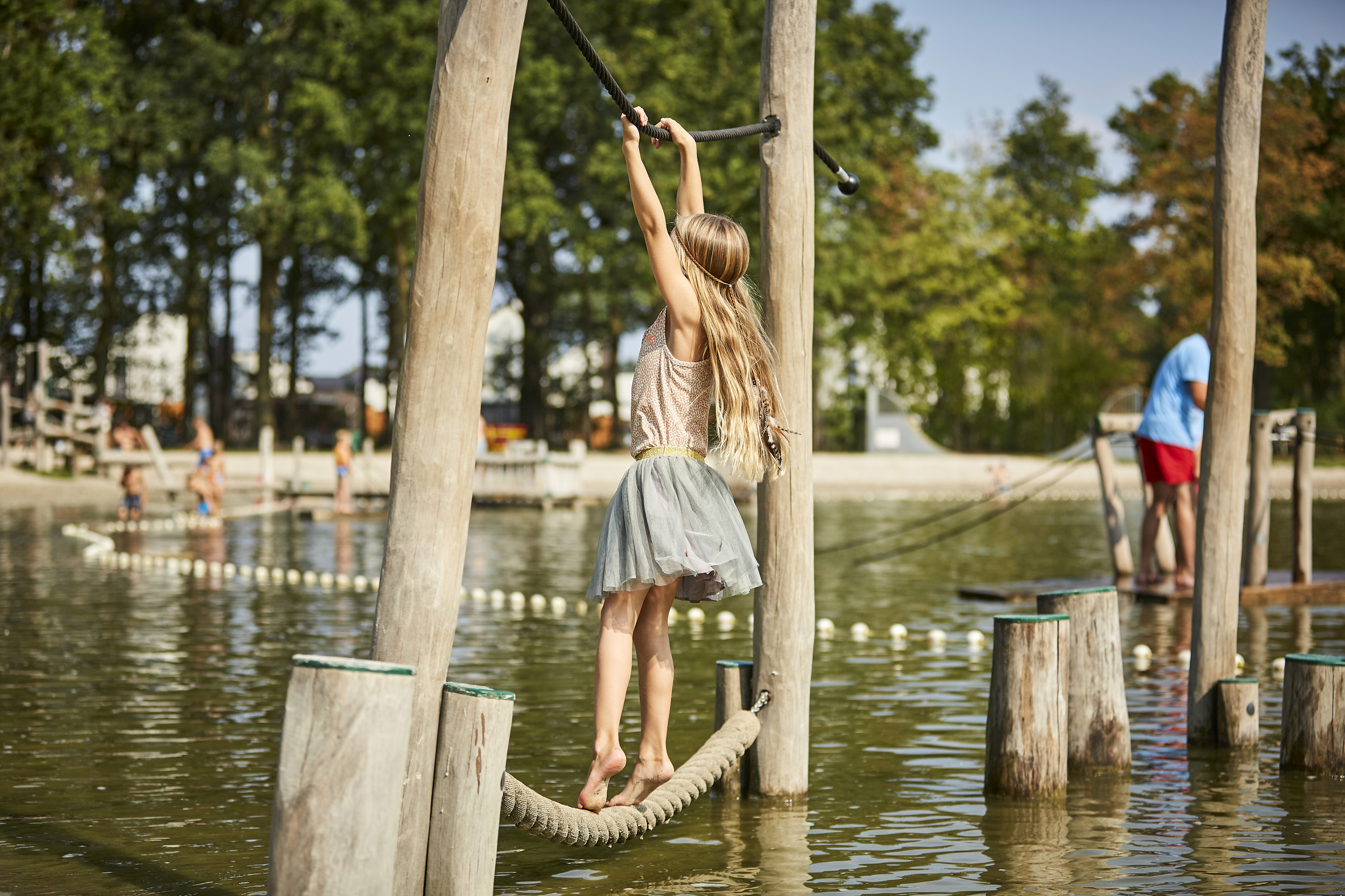 Een meisje met lang haar balanceert op een touwparcours boven het water in de avontuurlijke waterspeeltuin van De Leistert.
