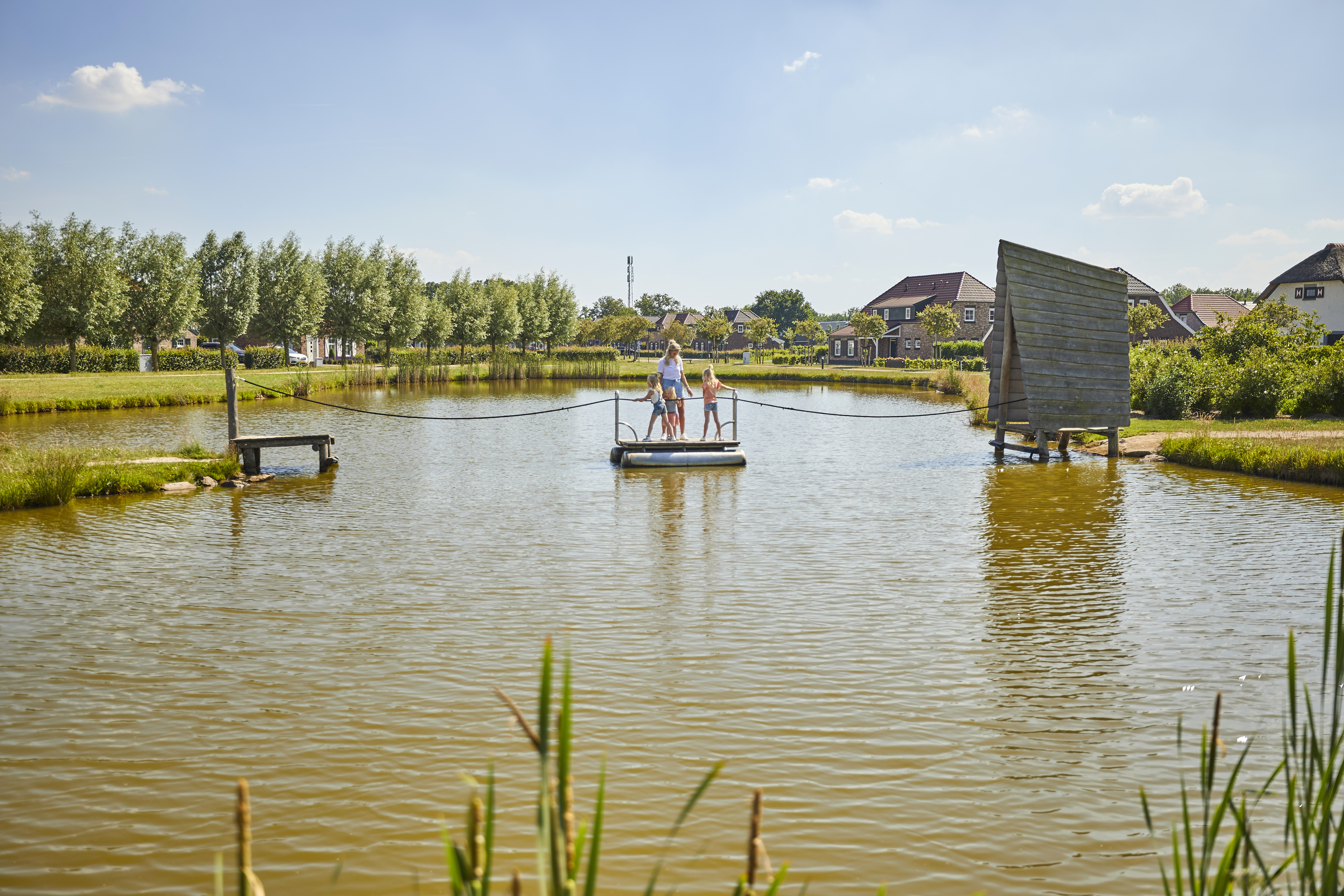 Drie kinderen staan op een houten trekvlot en trekken zichzelf naar de overkant van de roei- en speelvijver op Recreatiepark De Leistert.