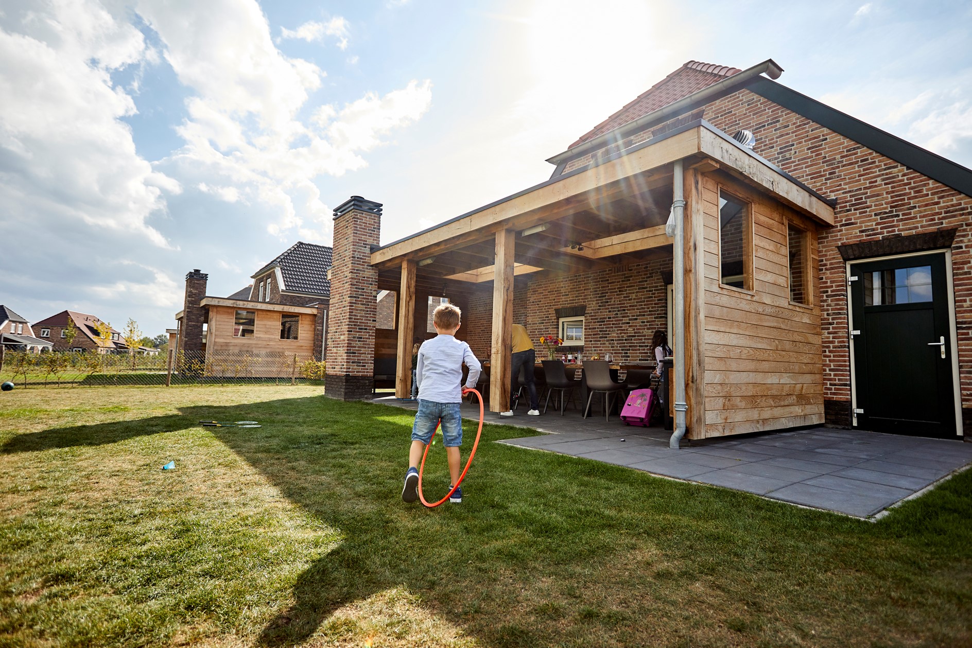 Een jongen speelt met een hoepel op het grote grasveld achter een luxe, houten vakantieboerderij op Recreatiepark De Leistert.