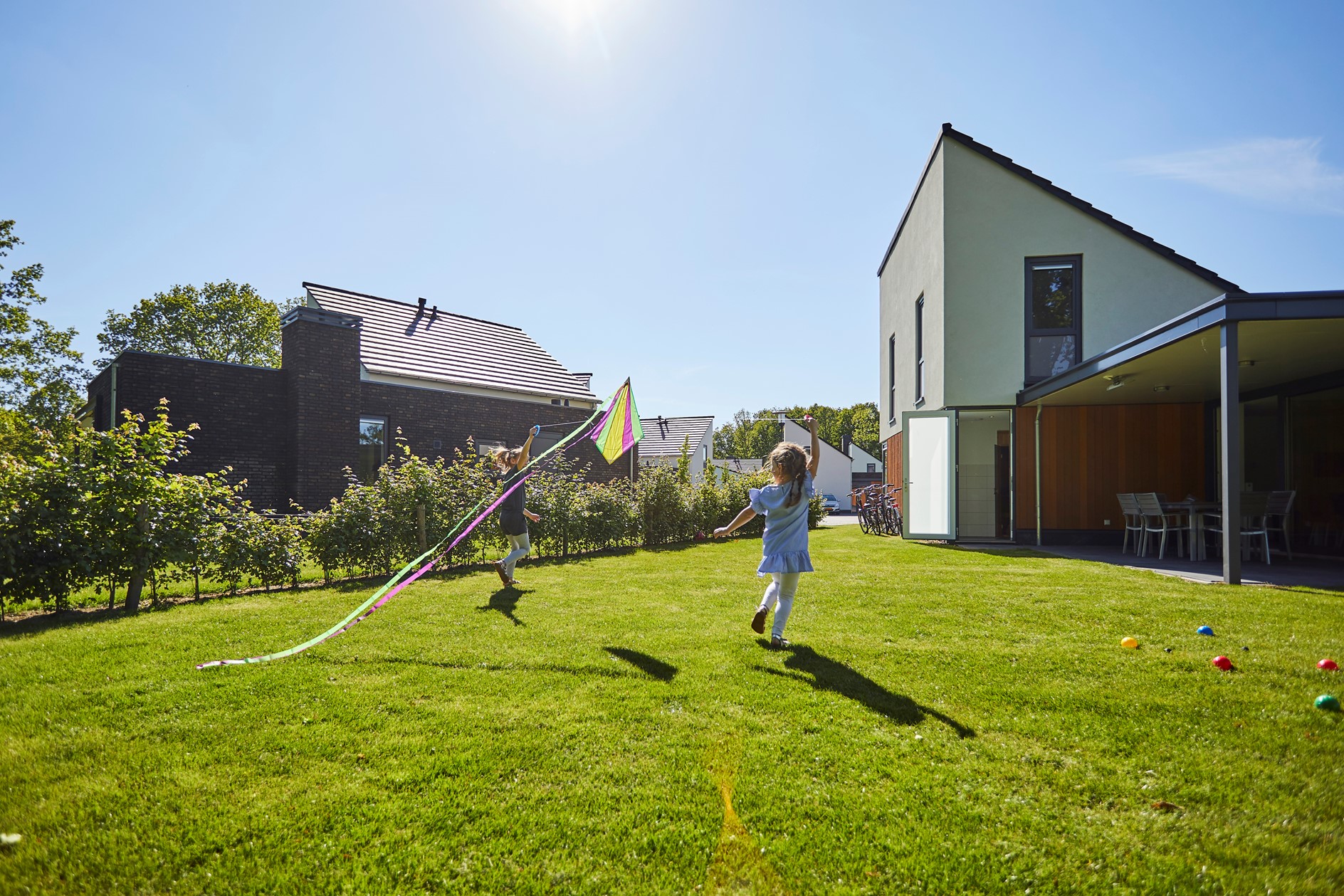 Een kind rent met een vlieger door de grote, zonnige tuin van een modern vakantiehuis op Recreatiepark De Leistert.