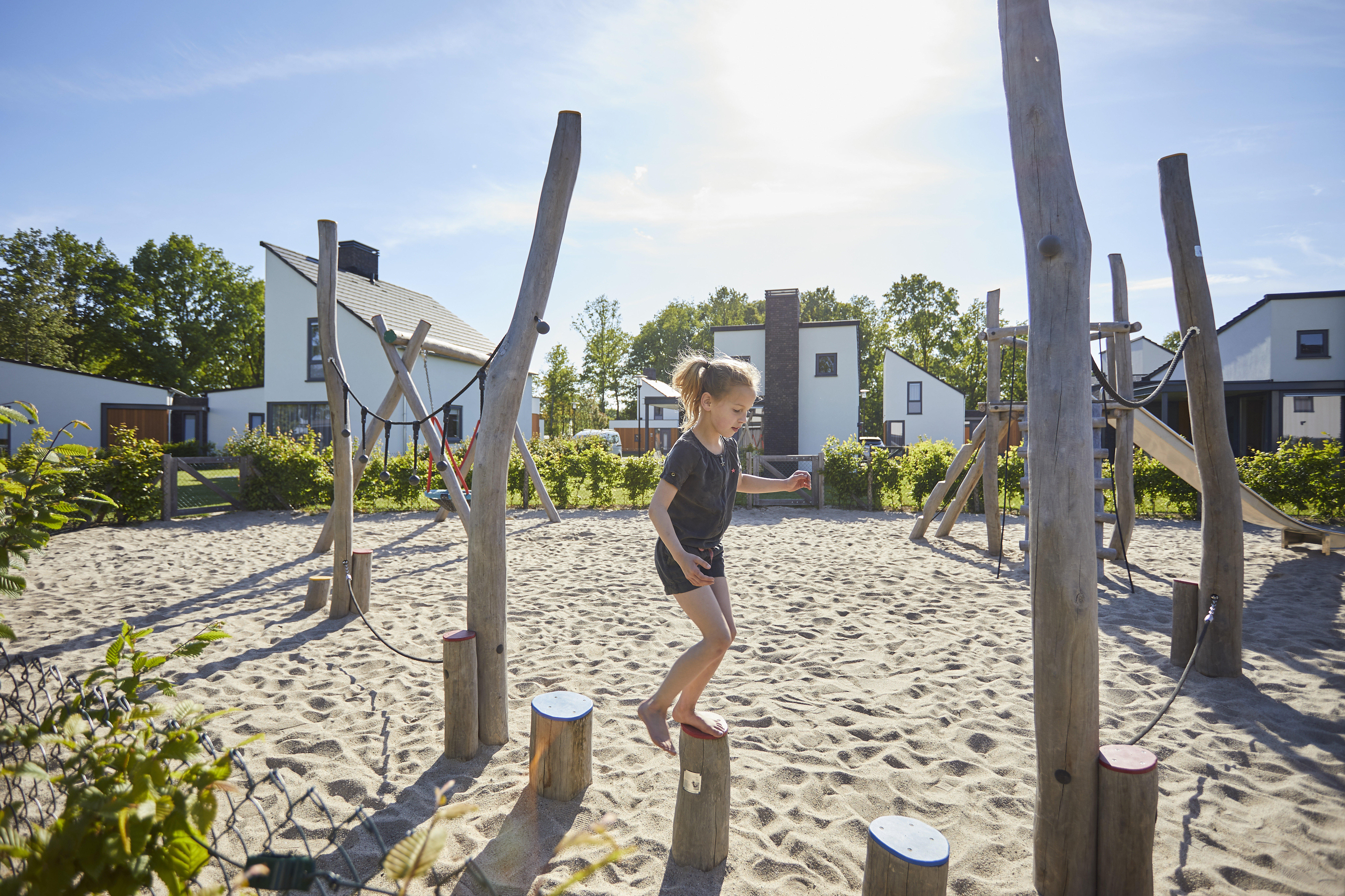 Een meisje balanceert op houten paaltjes in de zandspeeltuin die tussen de moderne vakantiehuizen van De Leistert ligt.