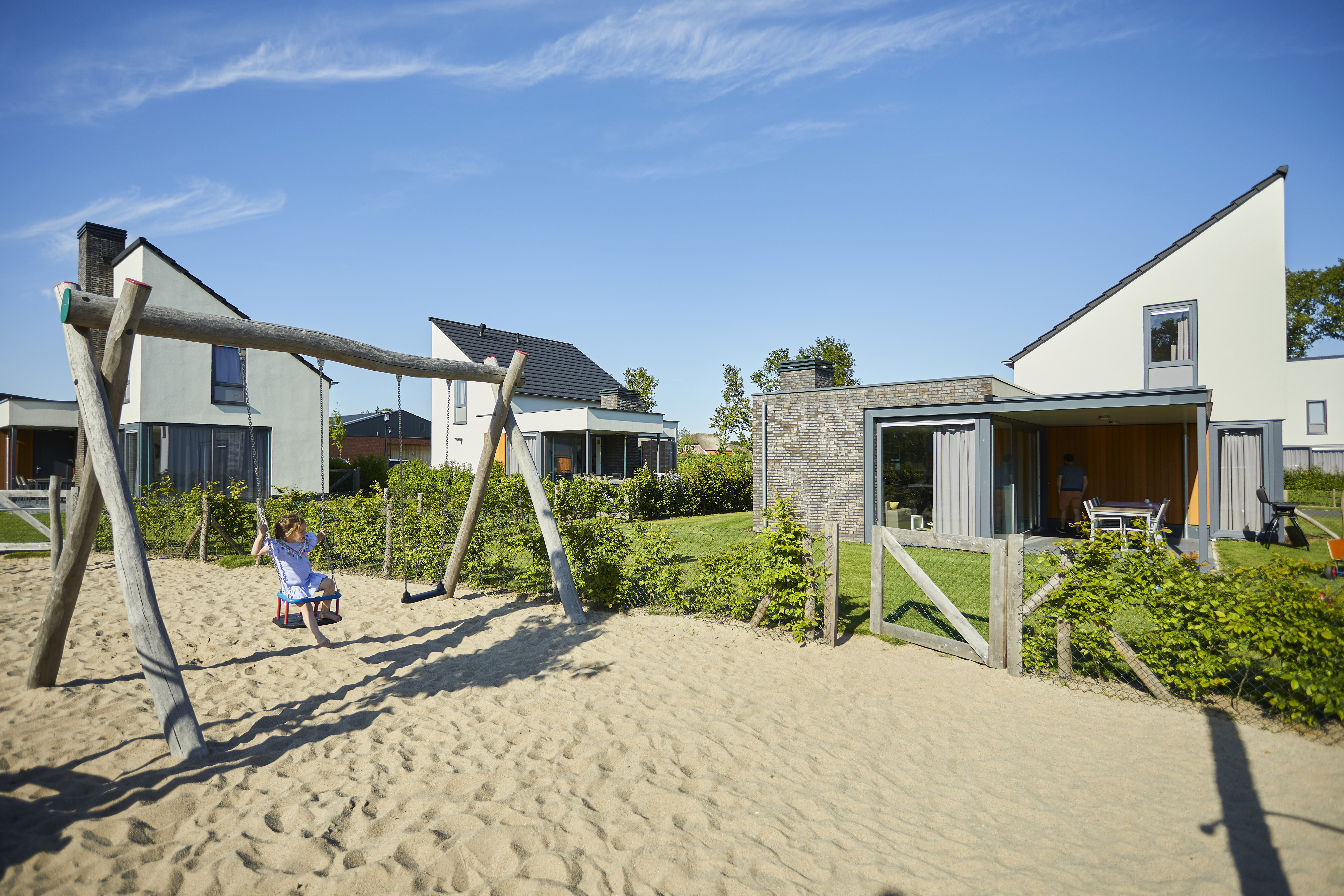Een kind schommelt in de zandspeeltuin die direct gelegen is bij de moderne vakantiehuizen op Recreatiepark De Leistert.