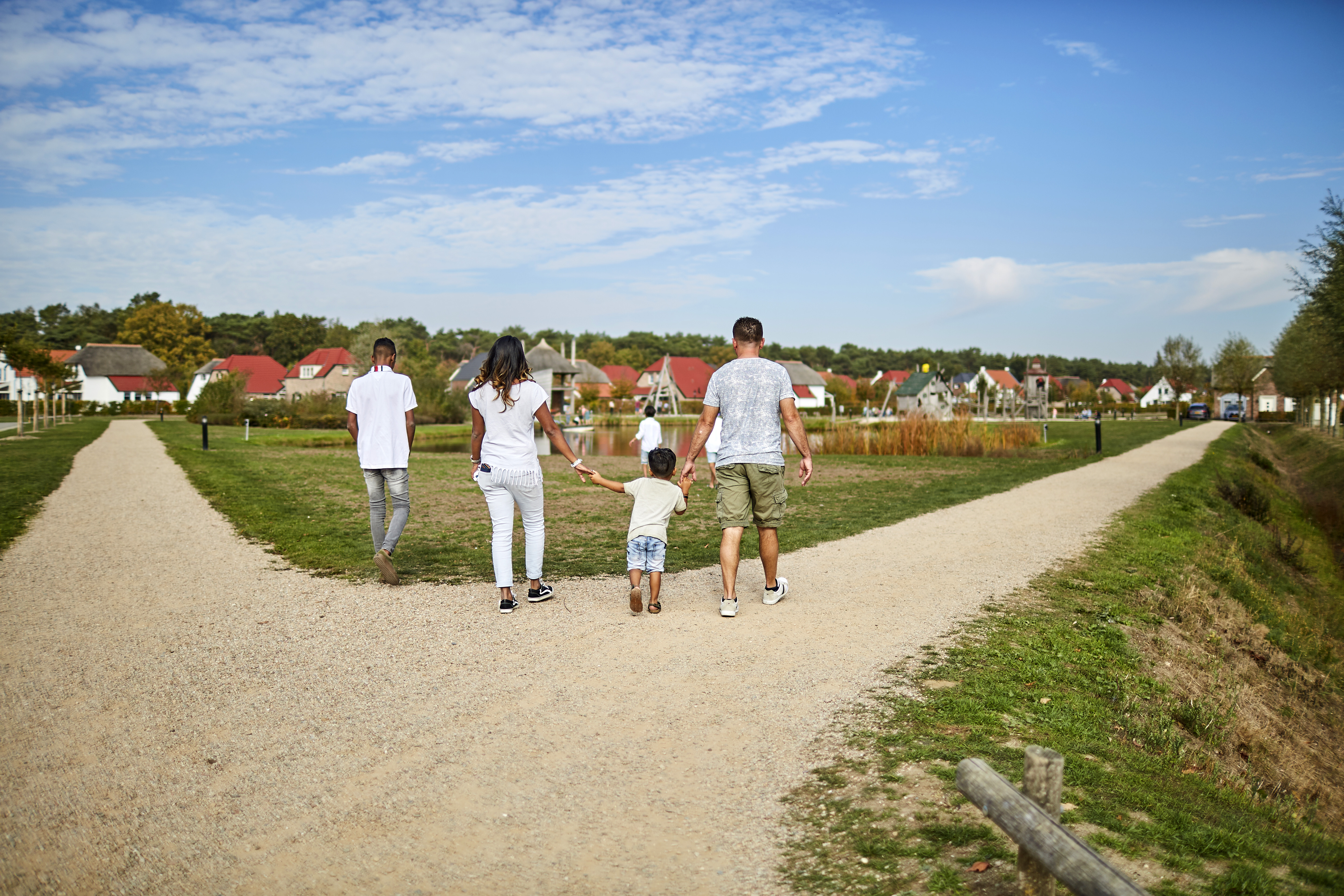 Een gezin met twee kinderen wandelt hand in hand over een onverhard pad op het uitgestrekte terrein van Recreatiepark De Leistert.