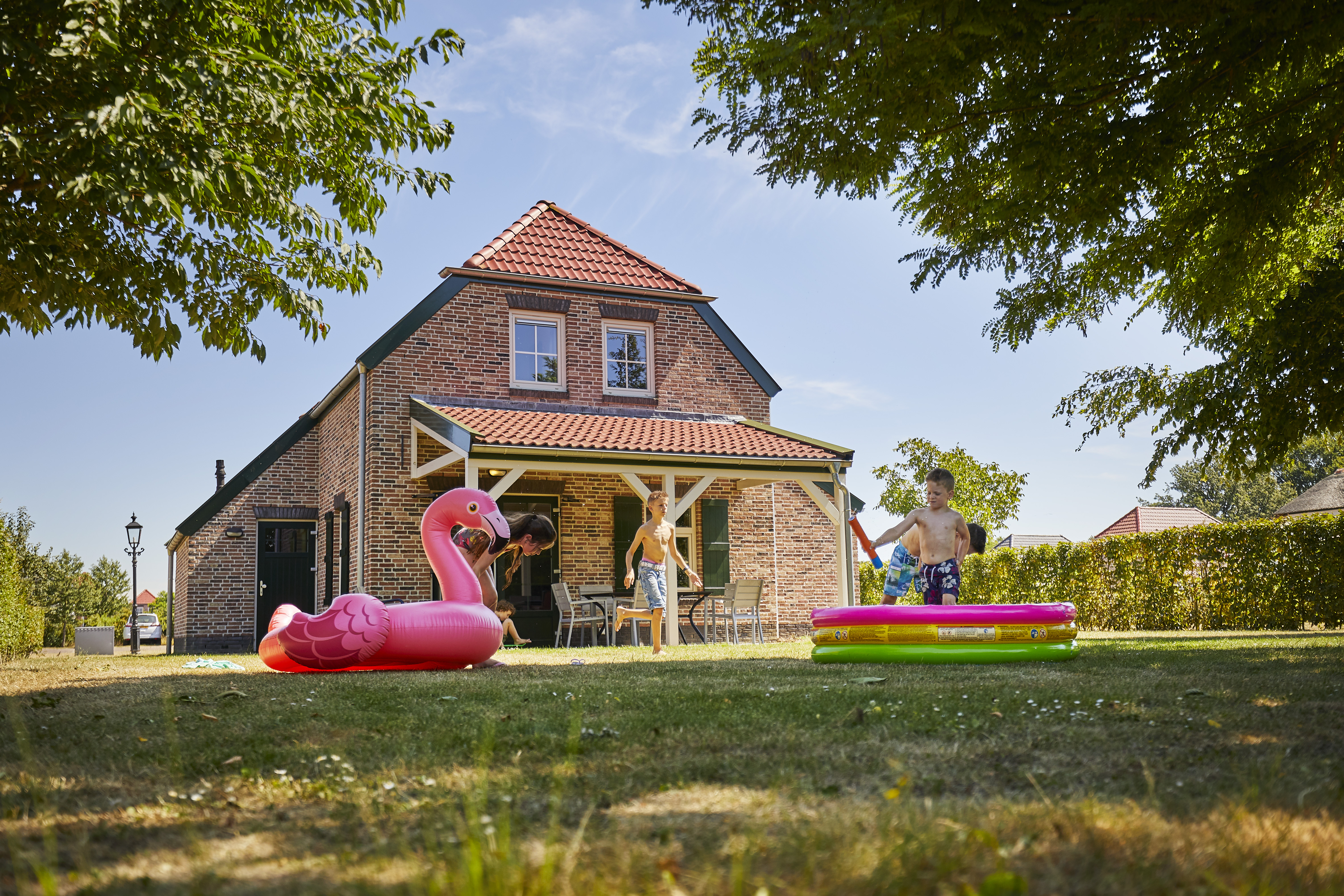 Kinderen spelen in een opblaasbaar zwembadje in de tuin van een vakantieboerderij, met een grote roze flamingo ernaast.