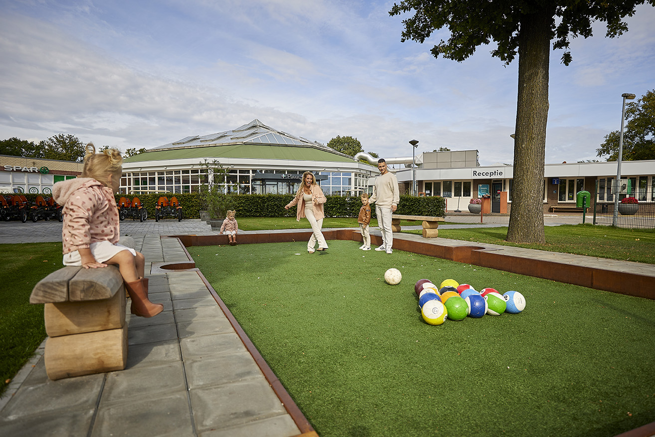 Een familie speelt een potje voetbalbiljart op de speciale baan op het buitenterrein van Recreatiepark De Leistert, bij het overdekte terras.