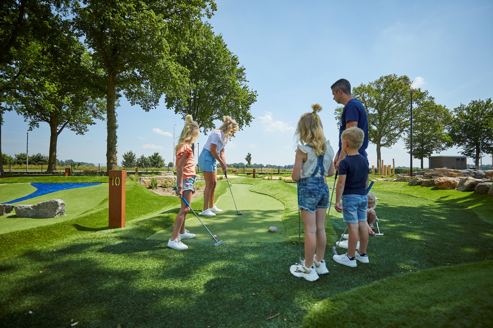 Een gezin met drie kinderen speelt midgetgolf op de avontuurlijke en groen aangelegde golfbaan van Recreatiepark De Leistert.