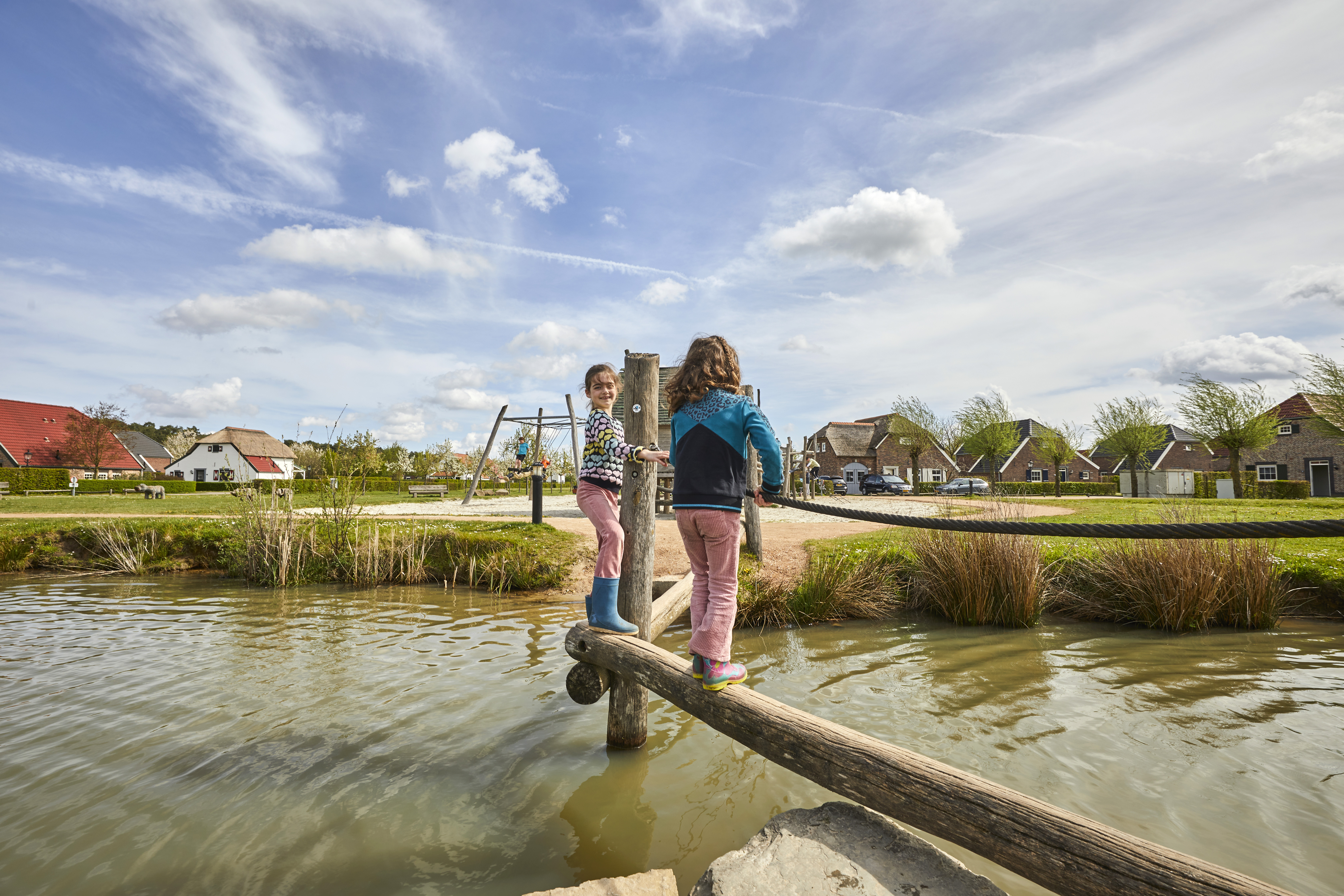 Twee meisjes balanceren op een houten boomstam over de speelvijver op Recreatiepark De Leistert.
