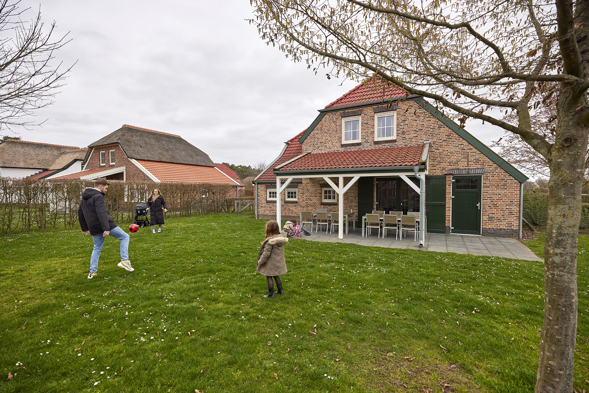 Een familie speelt samen op het grote grasveld voor hun vakantieboerderij op Recreatiepark De Leistert.