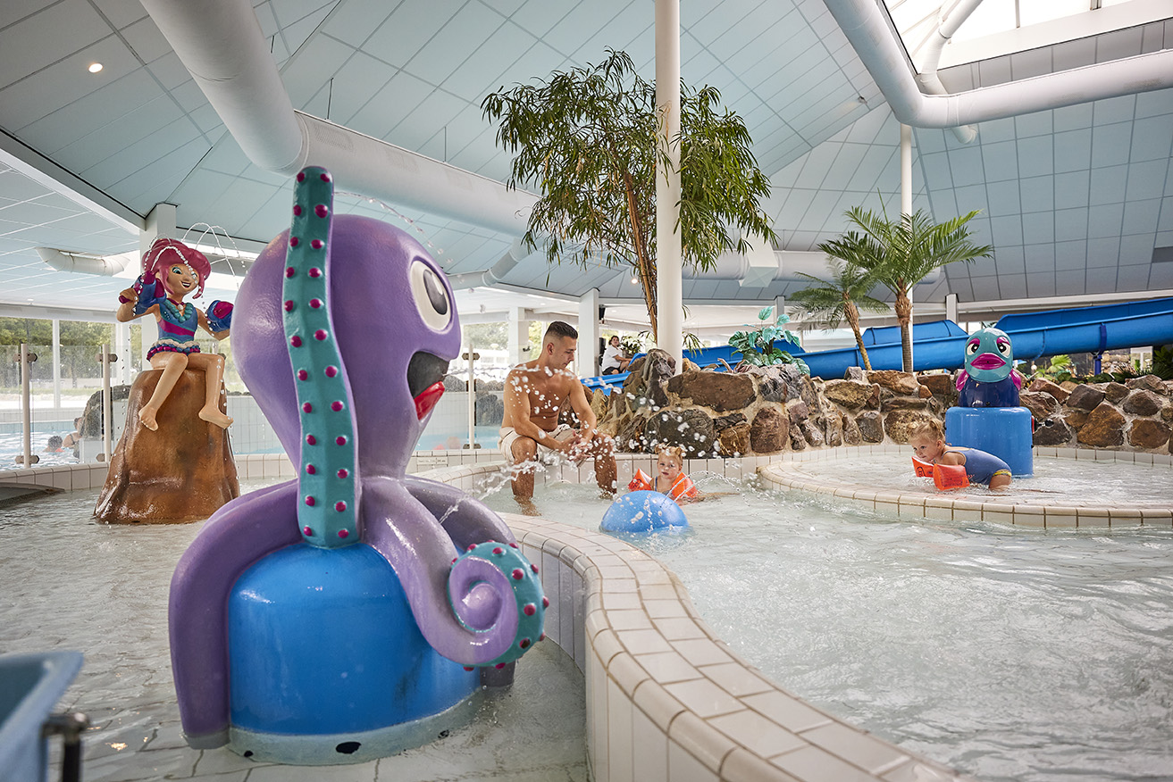 Kinderen spelen in het kinder-doe-bad van het subtropisch zwembad op Recreatiepark De Leistert, met een vrolijke paarse octopus en andere waterspeeltoestellen.