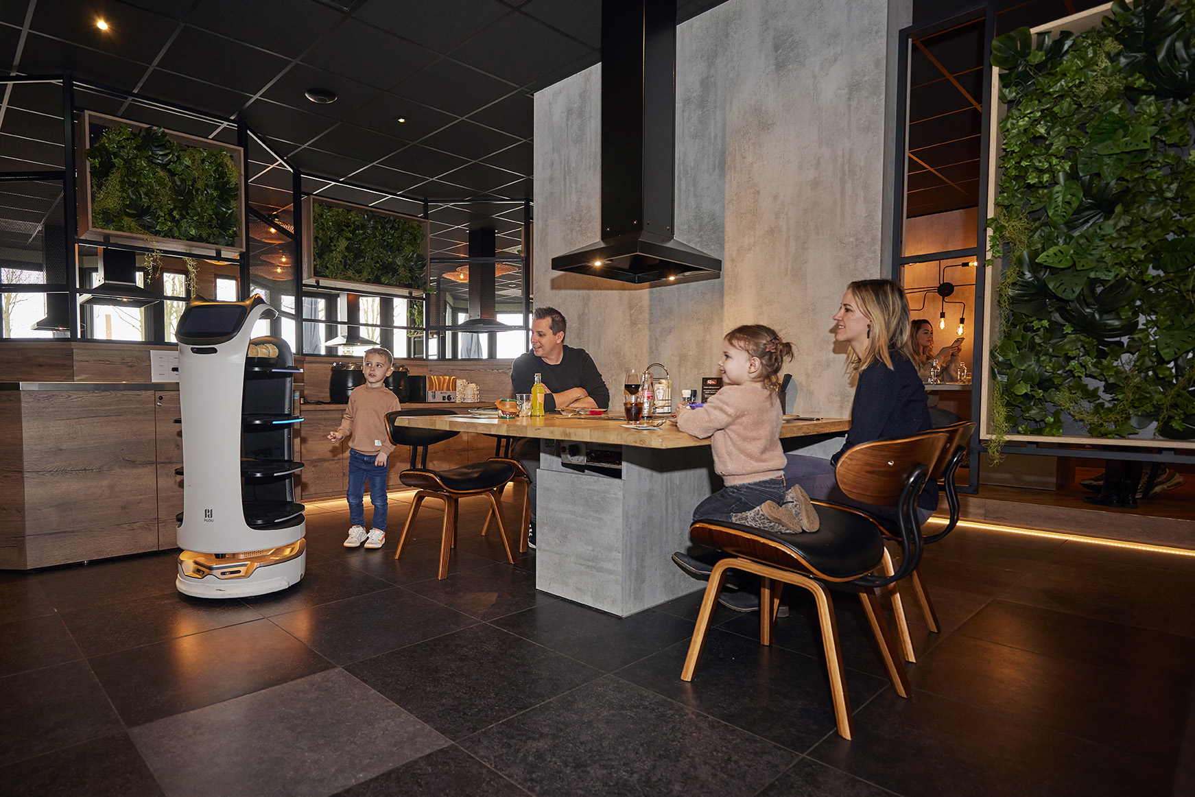 Een gezin met twee jonge kinderen wordt bediend door een rijdende serveerrobot in een modern restaurant op Recreatiepark De Leistert.