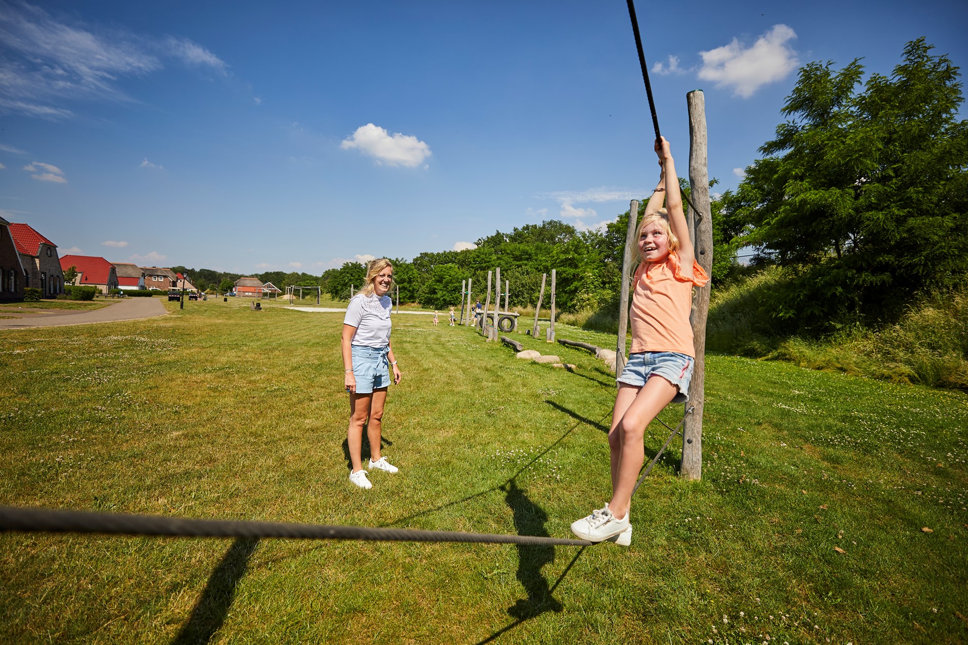 Een meisje zoeft aan de kabelbaan in de buitenspeeltuin van Recreatiepark De Leistert, terwijl een vriendinnetje kijkt.