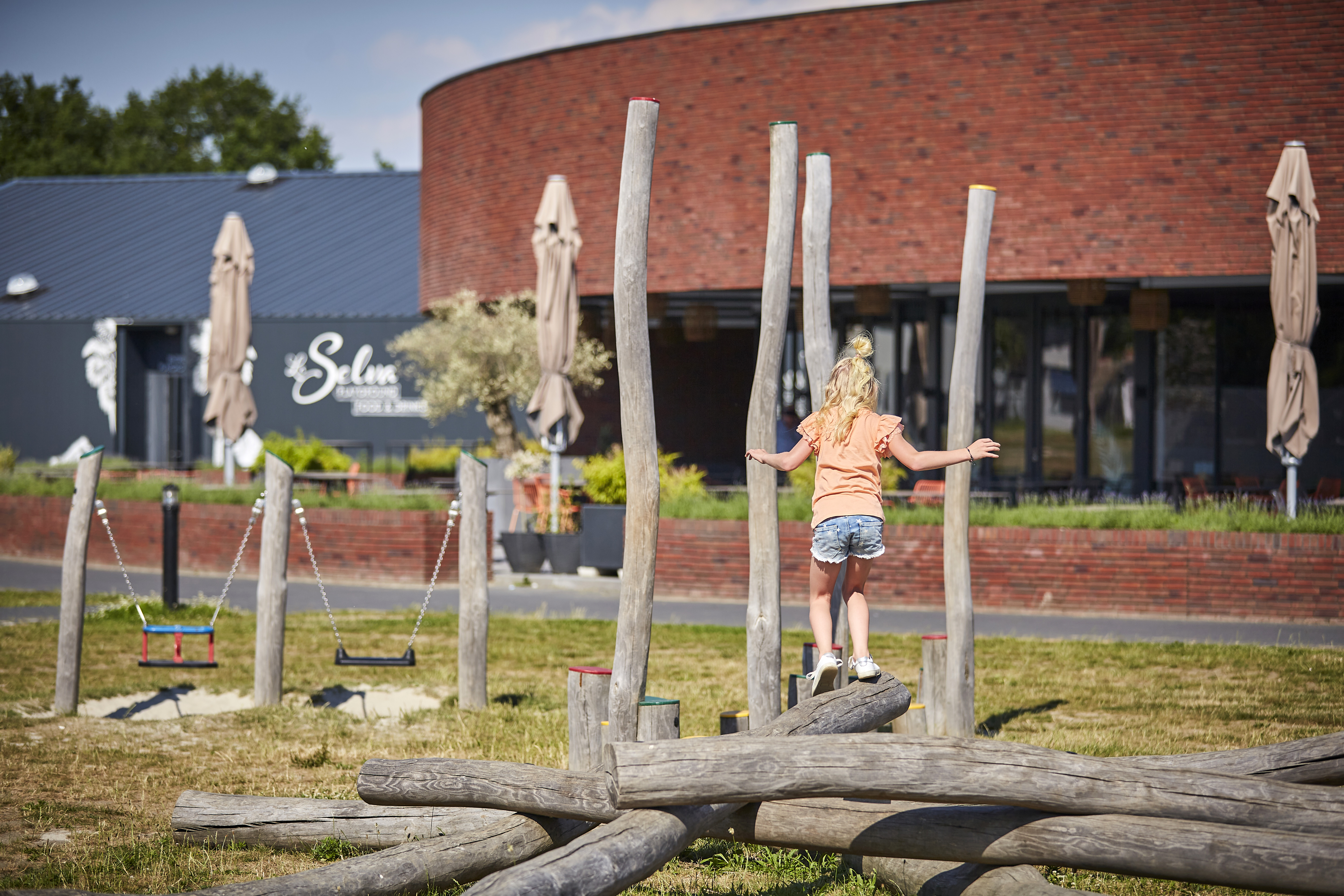 Een meisje balanceert op een houten evenwichtsbalk in de avontuurlijke buitenspeeltuin bij restaurant Buitenhof De Leistert.
