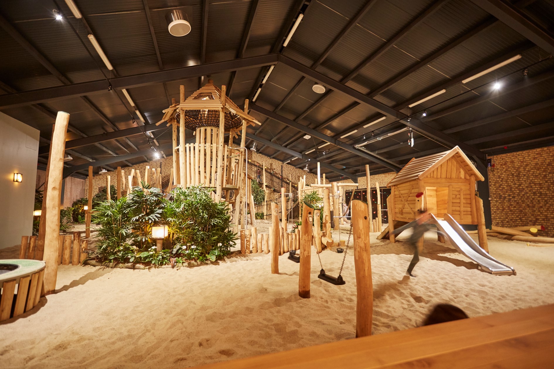 Overzicht van het grote indoor speelparadijs La Selva op Recreatiepark De Leistert, met houten klimtoestellen en een zandvloer.