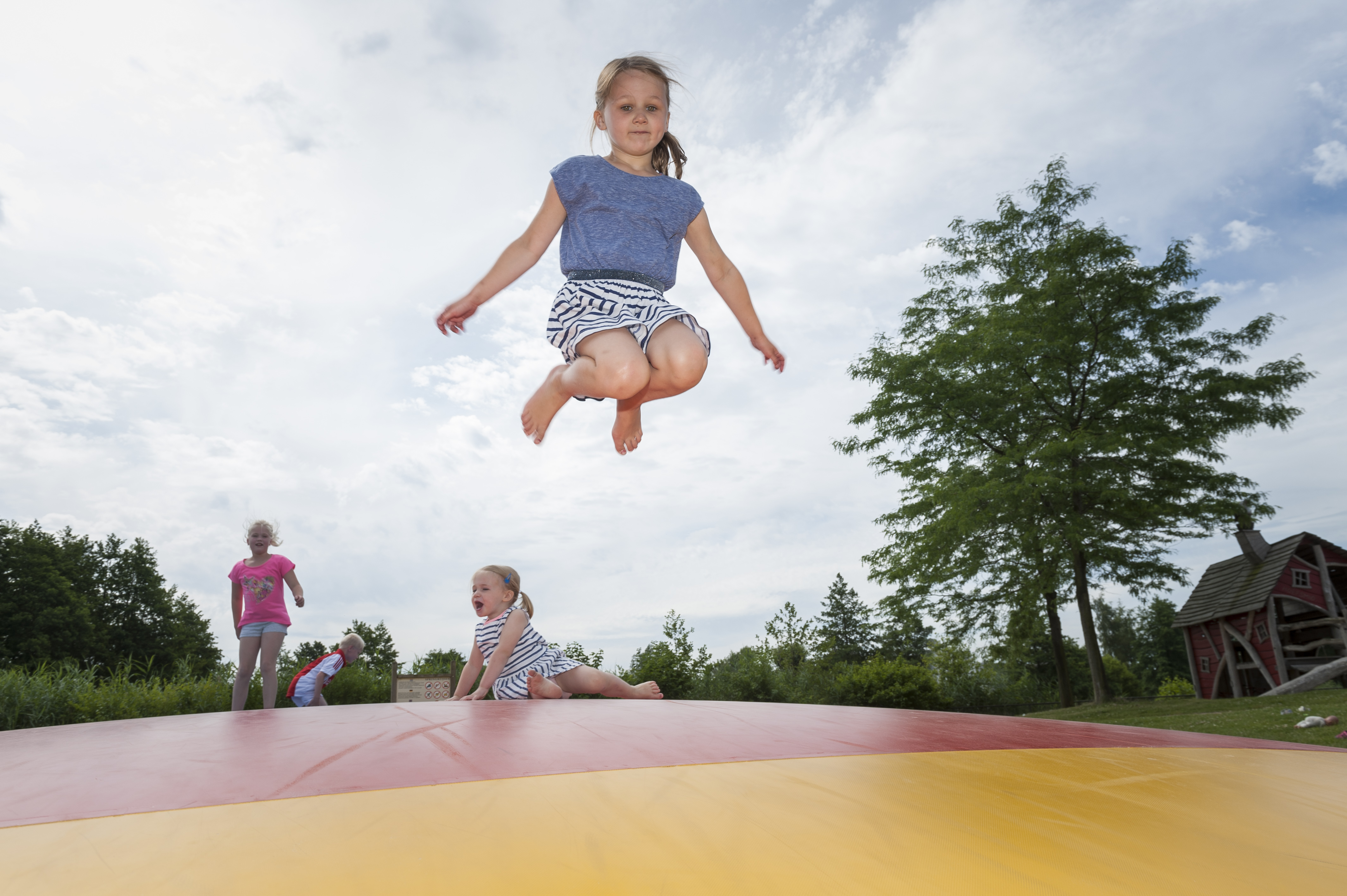 Kinderen maken hoge sprongen in de lucht op de grote, opblaasbare airtrampoline in de buitenspeeltuin van Landal Aelderholt.