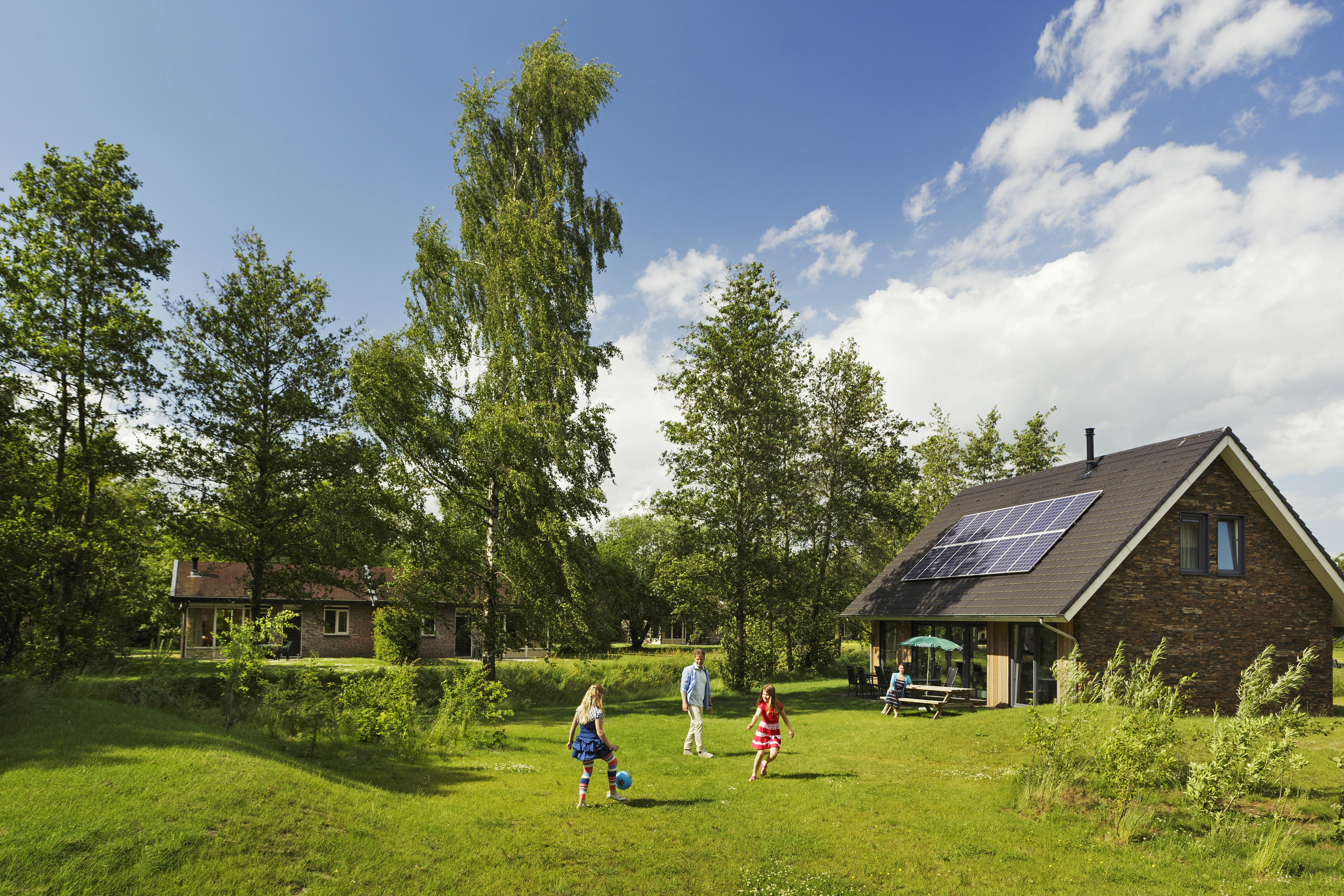Kinderen spelen en rennen op een groot, groen grasveld voor een vrijstaande bungalow met zonnepanelen op vakantiepark Landal Aelderholt.