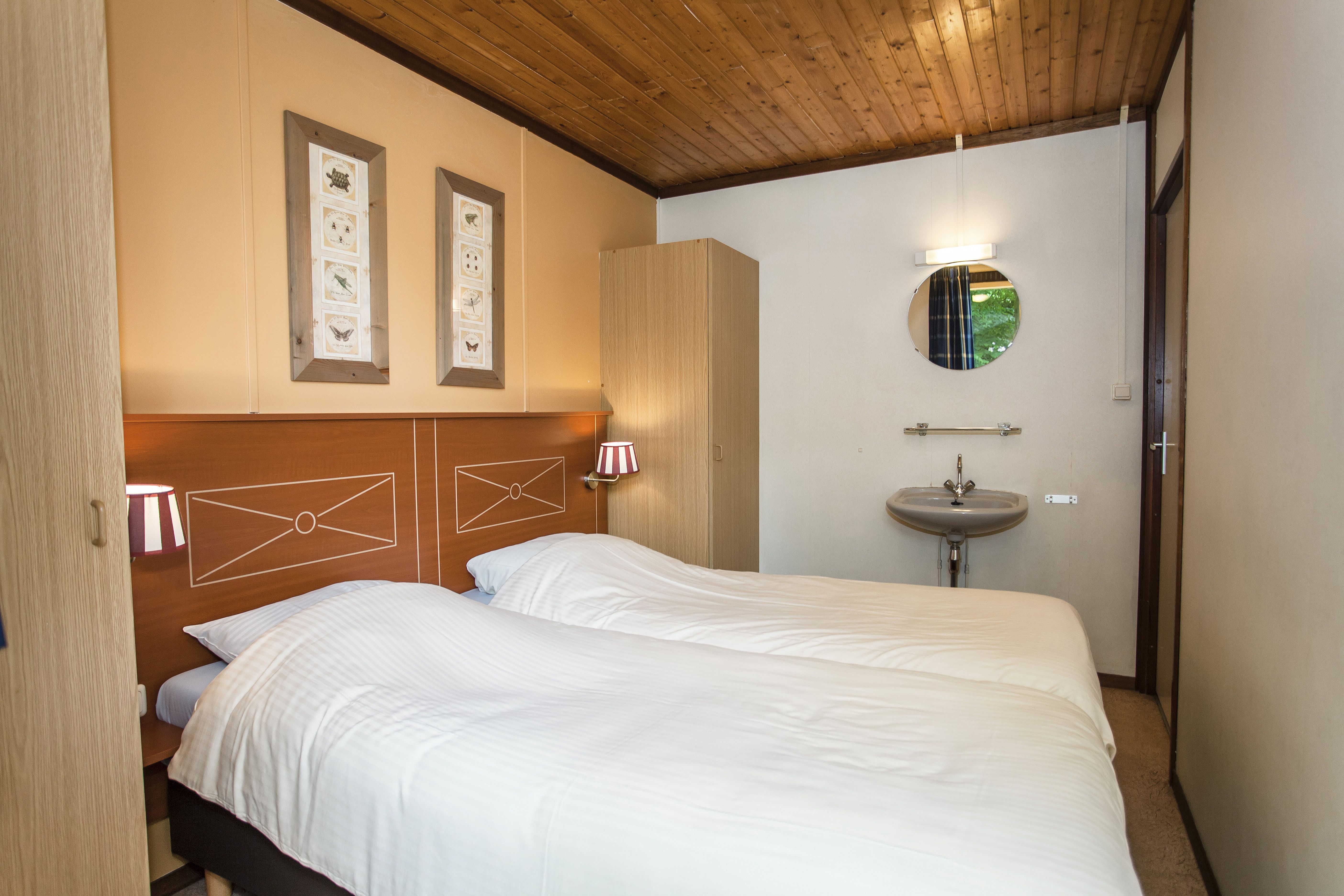Een netjes opgemaakt tweepersoonsbed in een sfeervolle slaapkamer met houten details en een eigen wastafel in een bungalow op Landal Aelderholt.