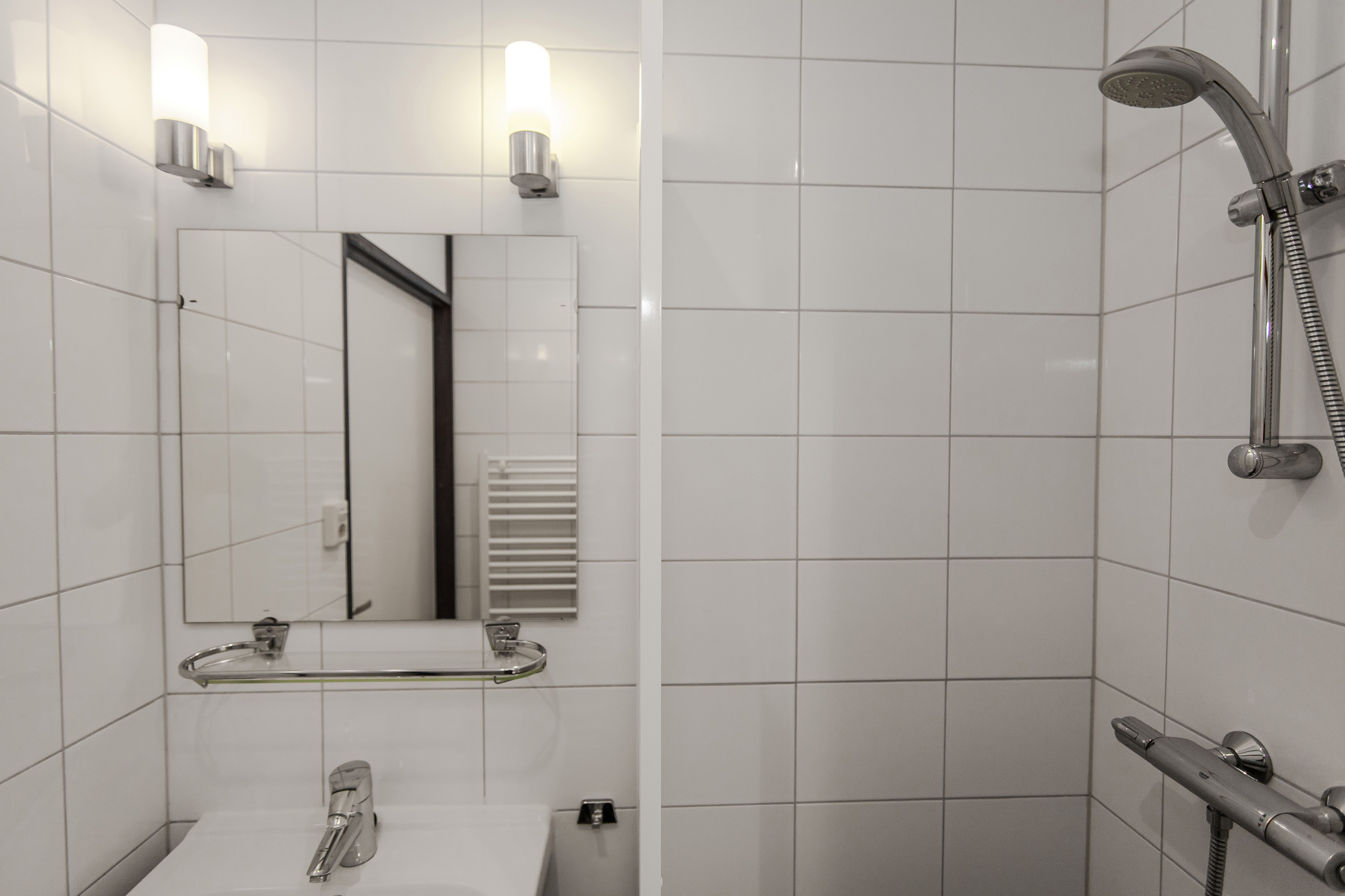 Een moderne badkamer met witte tegels, een wastafel, spiegel en een ruime inloopdouche in een bungalow op Landal Aelderholt in Drenthe.