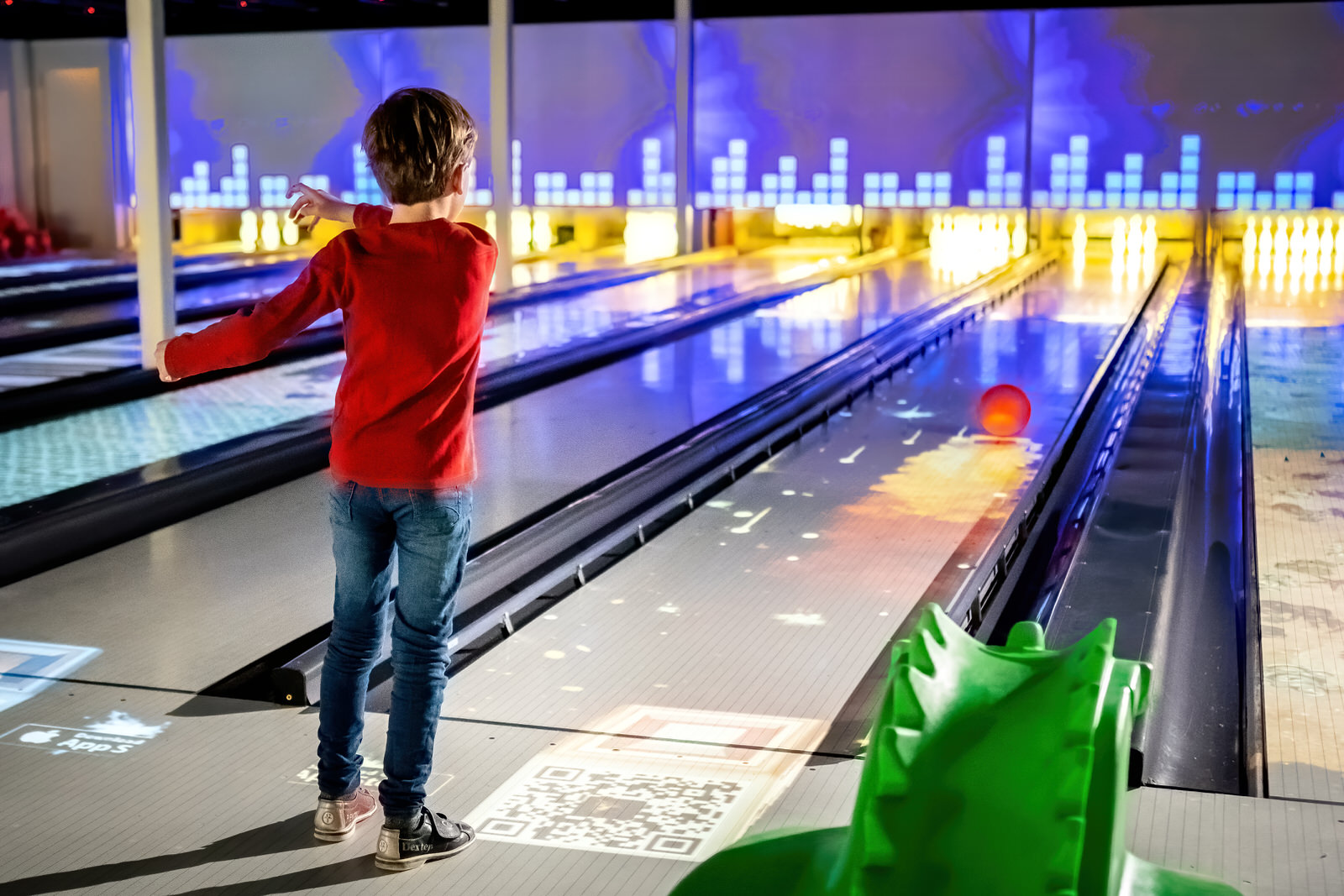 Kind gooit een bowlingbal op de hypermoderne, interactieve bowlingbaan met lichteffecten en een dinosaurus-hulpje op vakantiepark Landal De Lommerbergen.