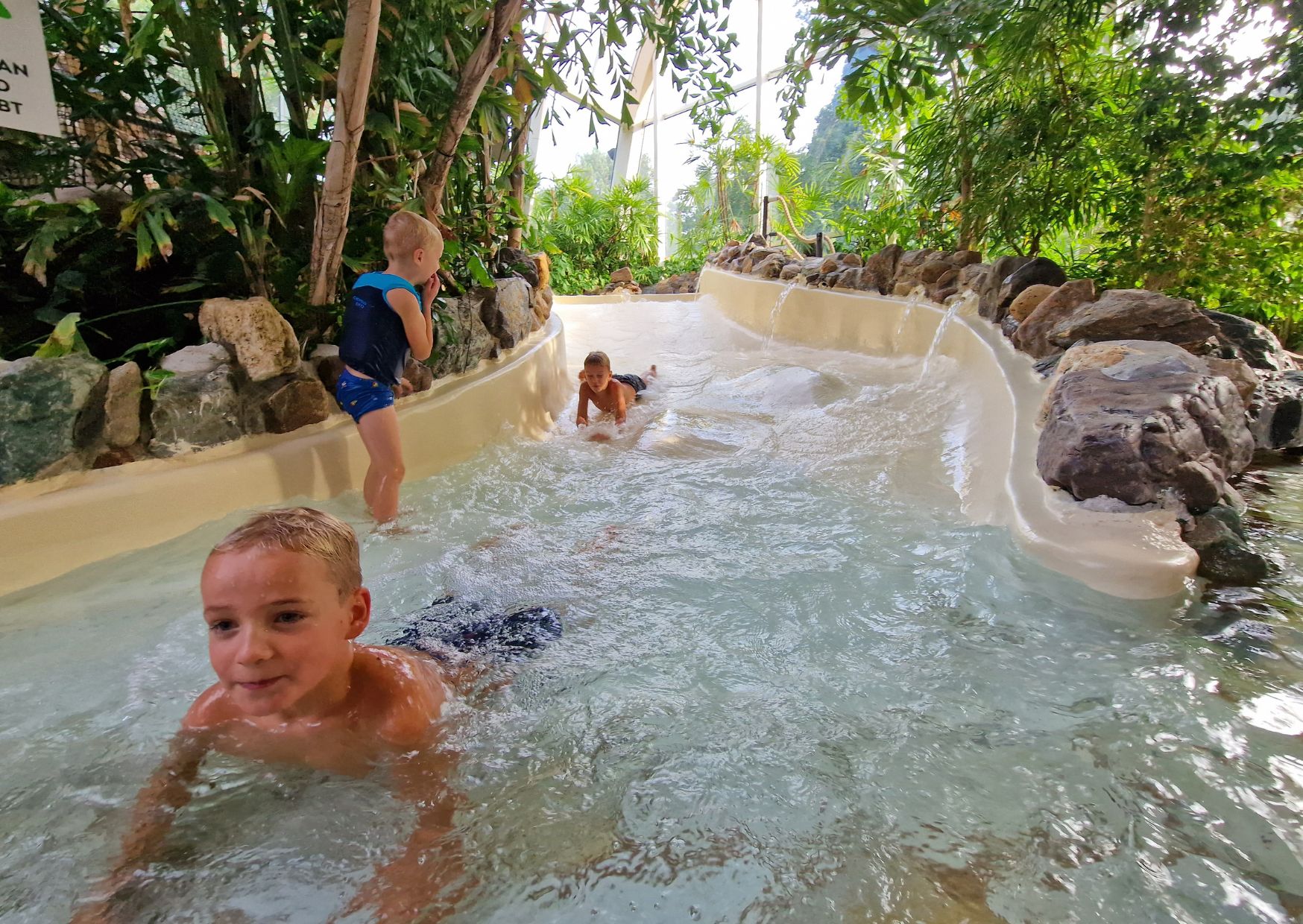 Kinderen laten zich meevoeren door de stroomversnelling van de wildwaterbaan die door een groene, tropische omgeving slingert bij Landal De Lommerbergen.