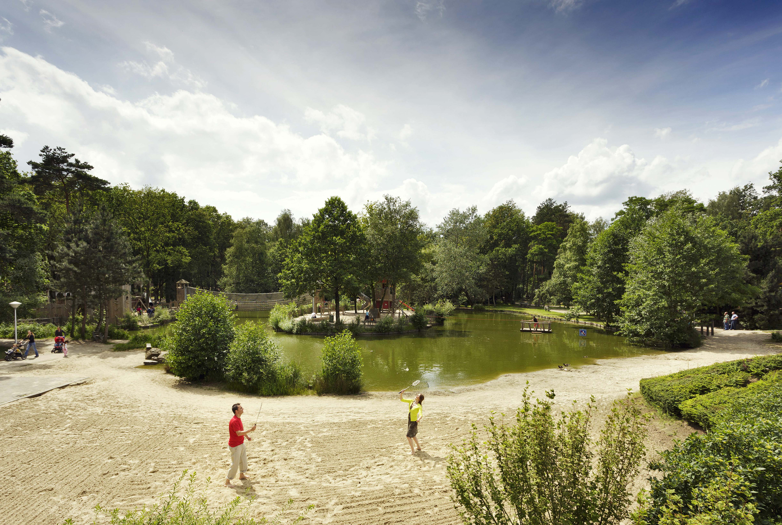 Kinderen spelen aan de rand van de grote speelvijver met zandstrand, omgeven door bomen, op het bosrijke vakantiepark Landal De Lommerbergen in Limburg.