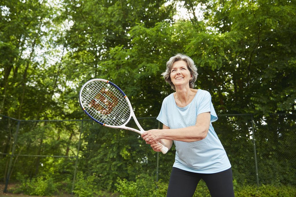 Een sportieve vrouw speelt een potje tennis op de outdoor tennisbaan van Landal De Wedderplassen.