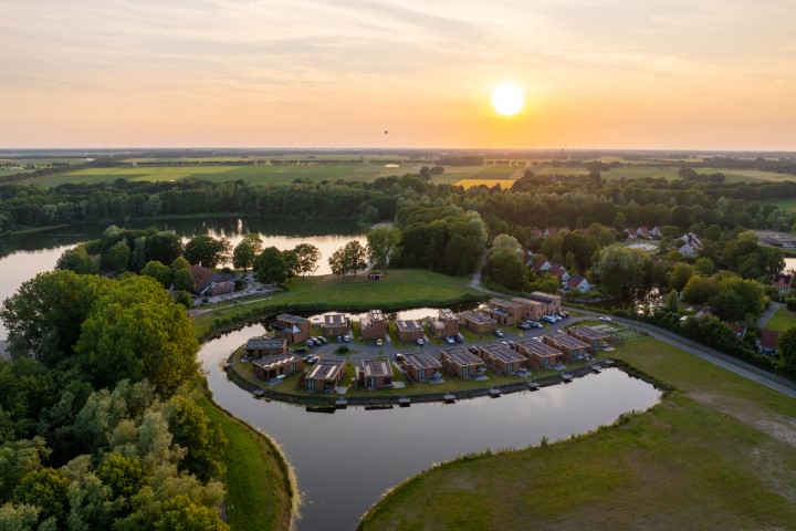 Een prachtige luchtfoto van Landal De Wedderplassen tijdens zonsondergang, waarbij de vakantiehuizen mooi oplichten aan het water.