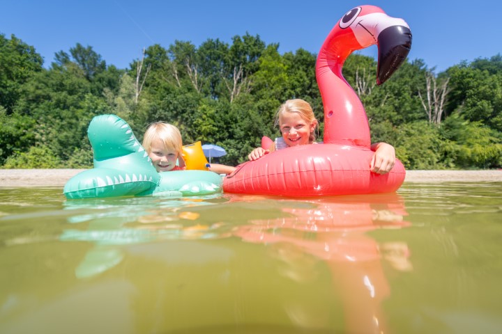 Twee blije kinderen dobberen op een grote opblaasbare roze flamingo in het recreatiemeer van Landal De Wedderplassen.