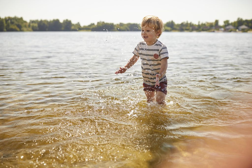 Een klein jongetje speelt en spettert in het ondiepe water van de Wedderplassen bij Landal.