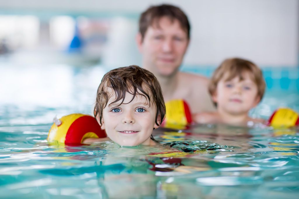 Een vader met zijn twee jonge kinderen, die zwemvleugels dragen, in het binnenzwembad van Landal De Wedderplassen.