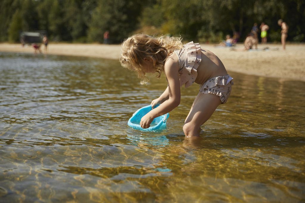 Klein meisje met krullen speelt met een schepje in het ondiepe water van de recreatieplas bij Landal De Wedderplassen.