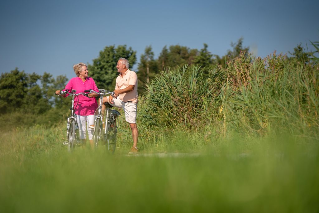 Opa en oma maken een wandeling met de fiets door het groene, natuurrijke landschap in de omgeving van Landal De Wedderplassen.