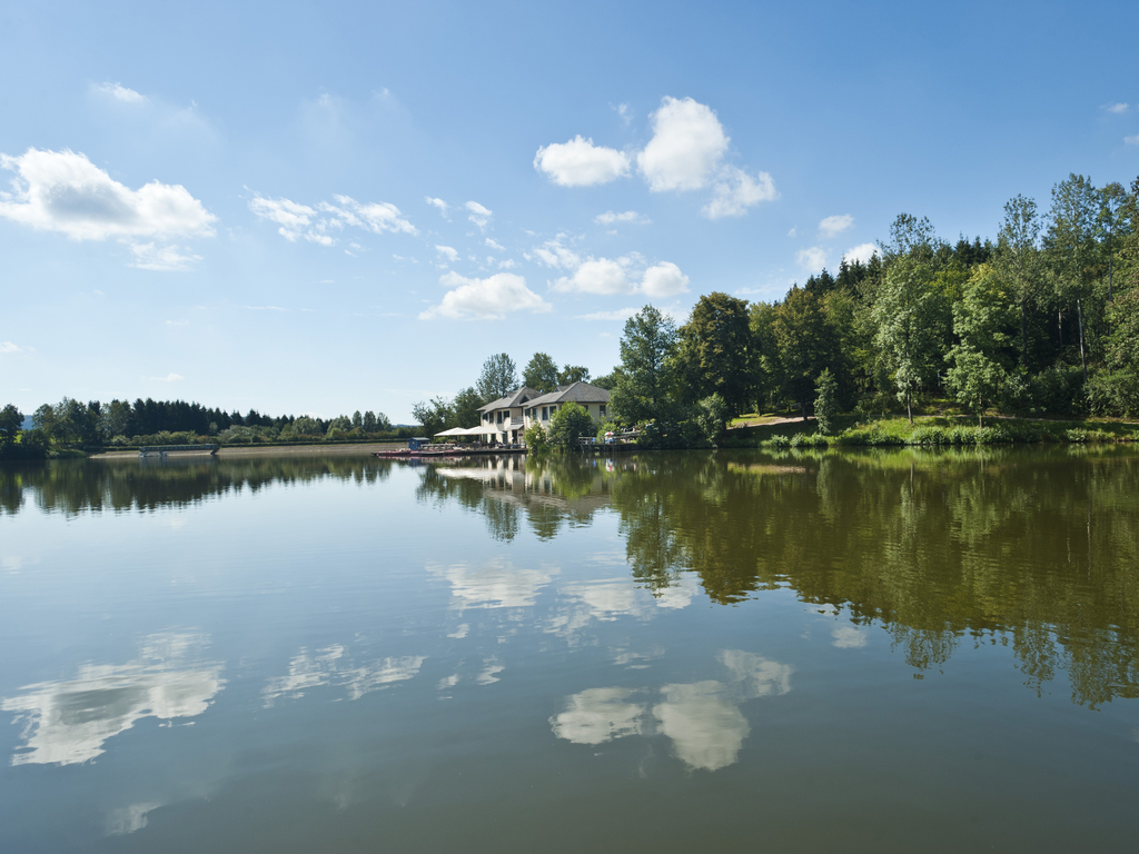 Het rustige stuwmeer bij Landal Hochwald op een zonnige dag, met de bomen en de blauwe lucht die weerspiegelen in het water.