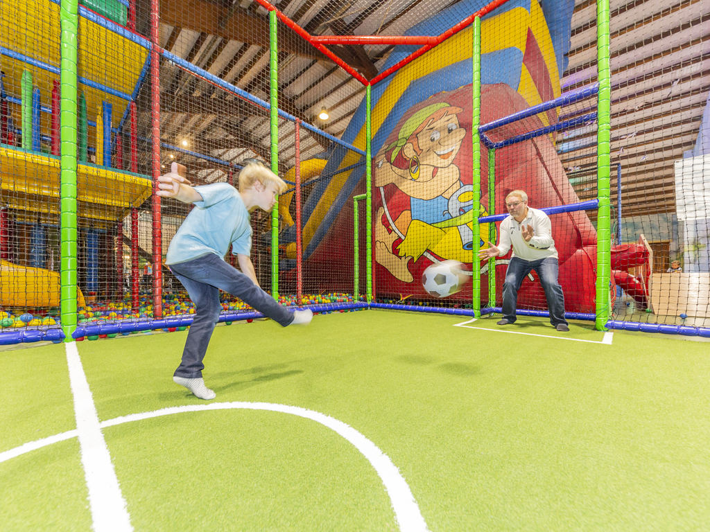 Twee jongens voetballen op het sportveldje in het kleurrijke indoorspeelparadijs van Landal Hochwald.