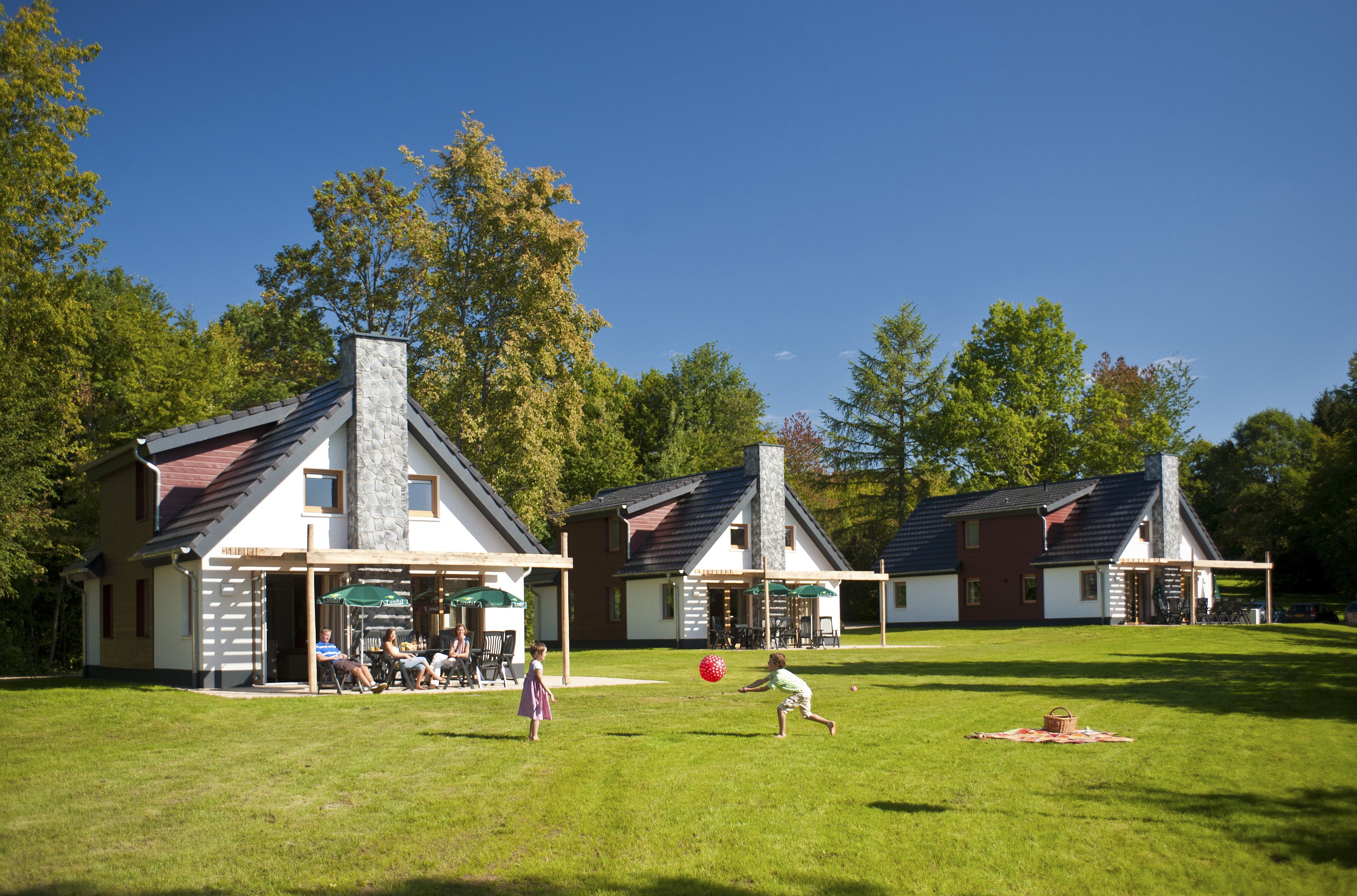Kinderen spelen met een bal op het grote, groene grasveld voor de vrijstaande vakantiebungalows op Landal Hochwald.