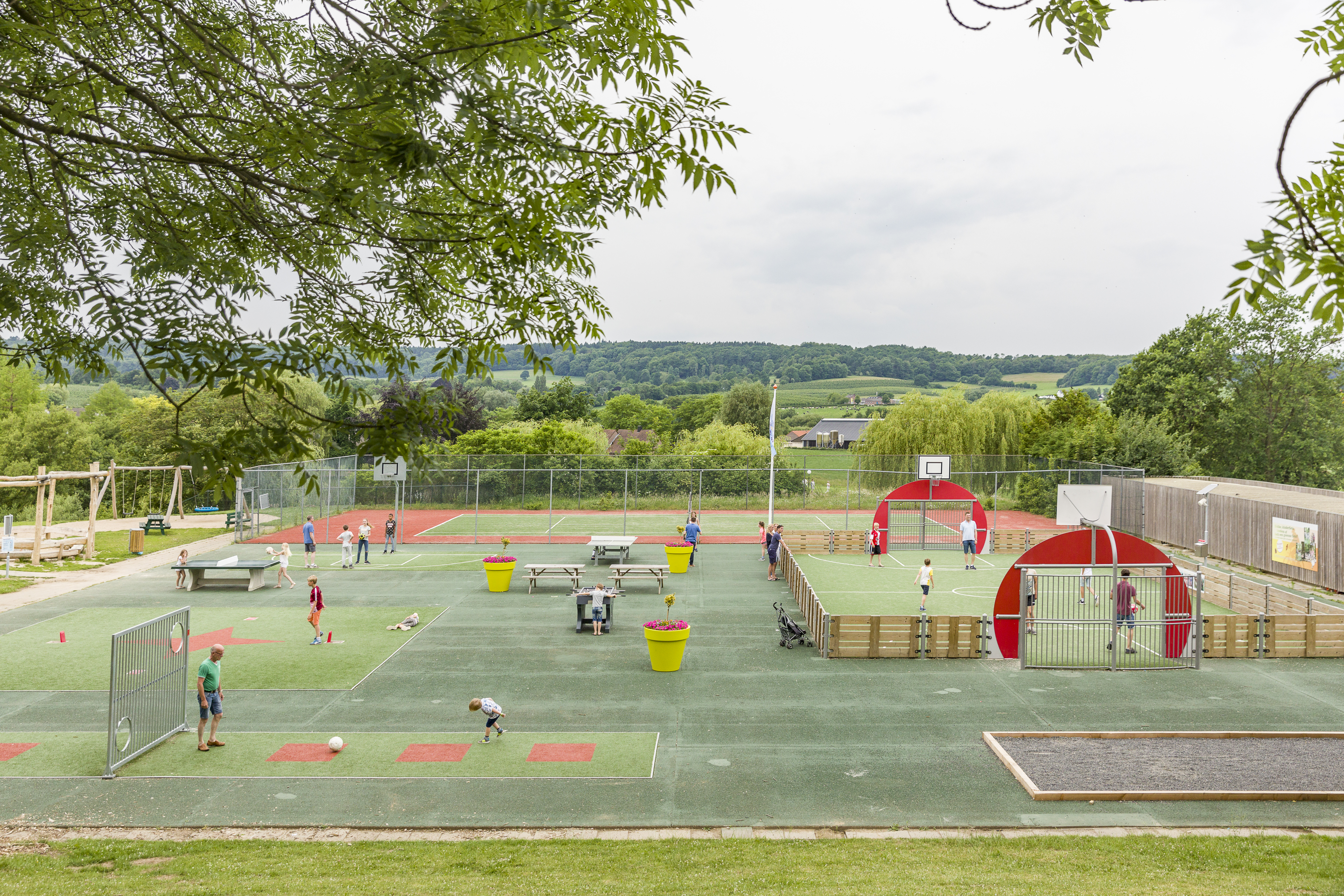 Kinderen spelen en sporten op het grote, multifunctionele sportveld met uitzicht op het heuvelachtige landschap van Limburg.