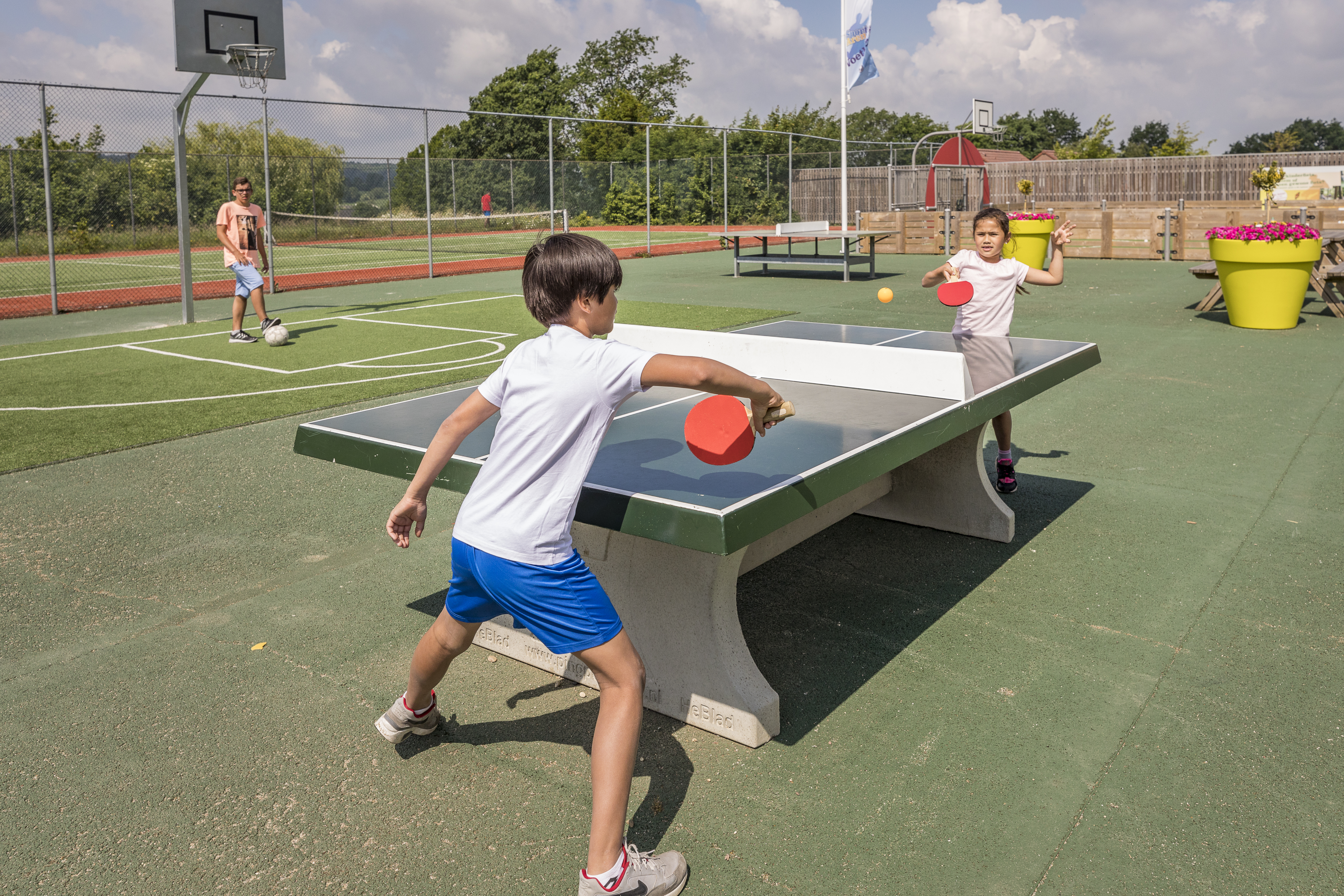 Twee jongens spelen een fanatiek potje tafeltennis op de buitentafeltennistafel op het sportveld van Landal Hoog Vaals.