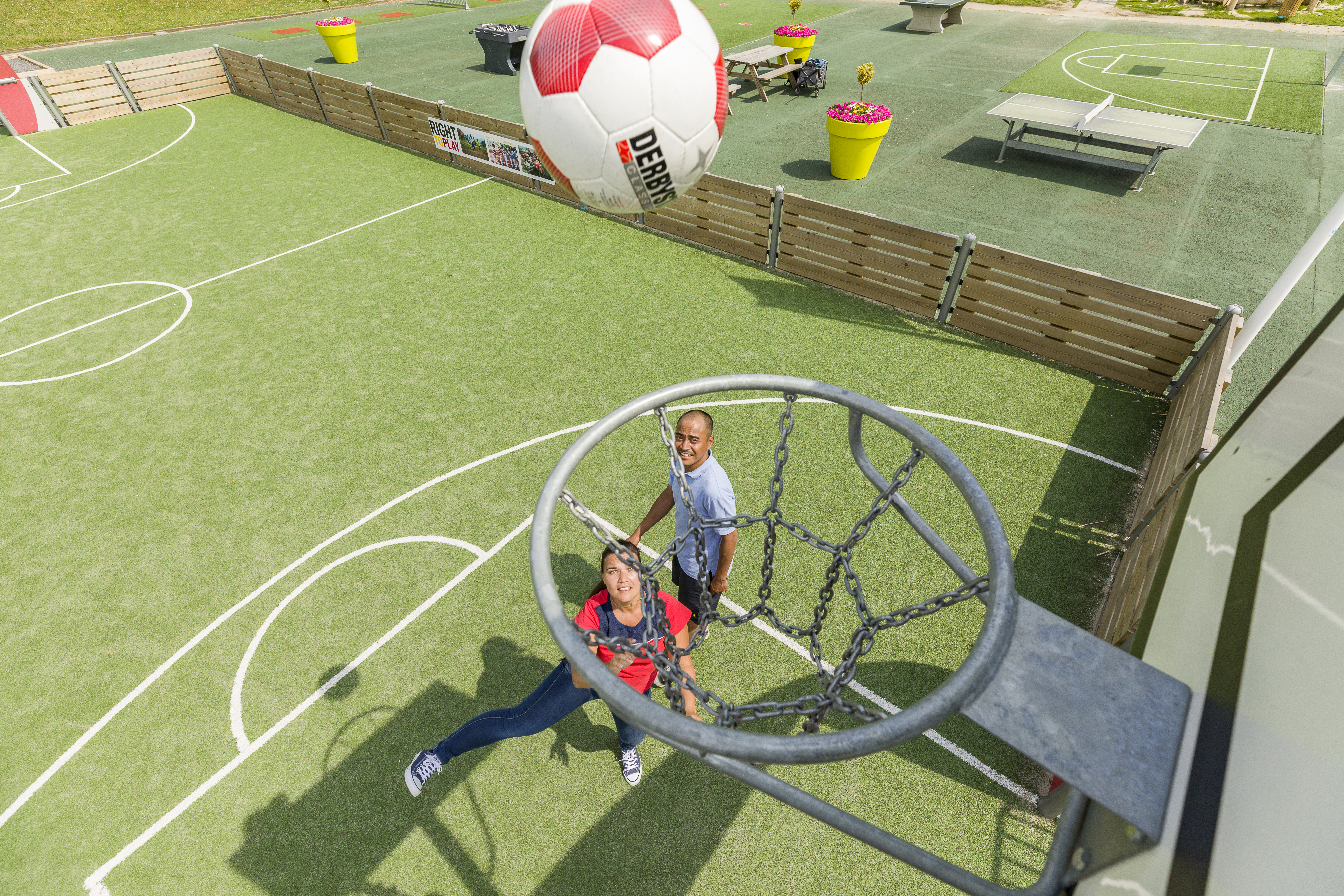 Een man en vrouw spelen een balspel op het sportveld, waarbij ze een enorme bal door een grote ring proberen te gooien op Landal Hoog Vaals.