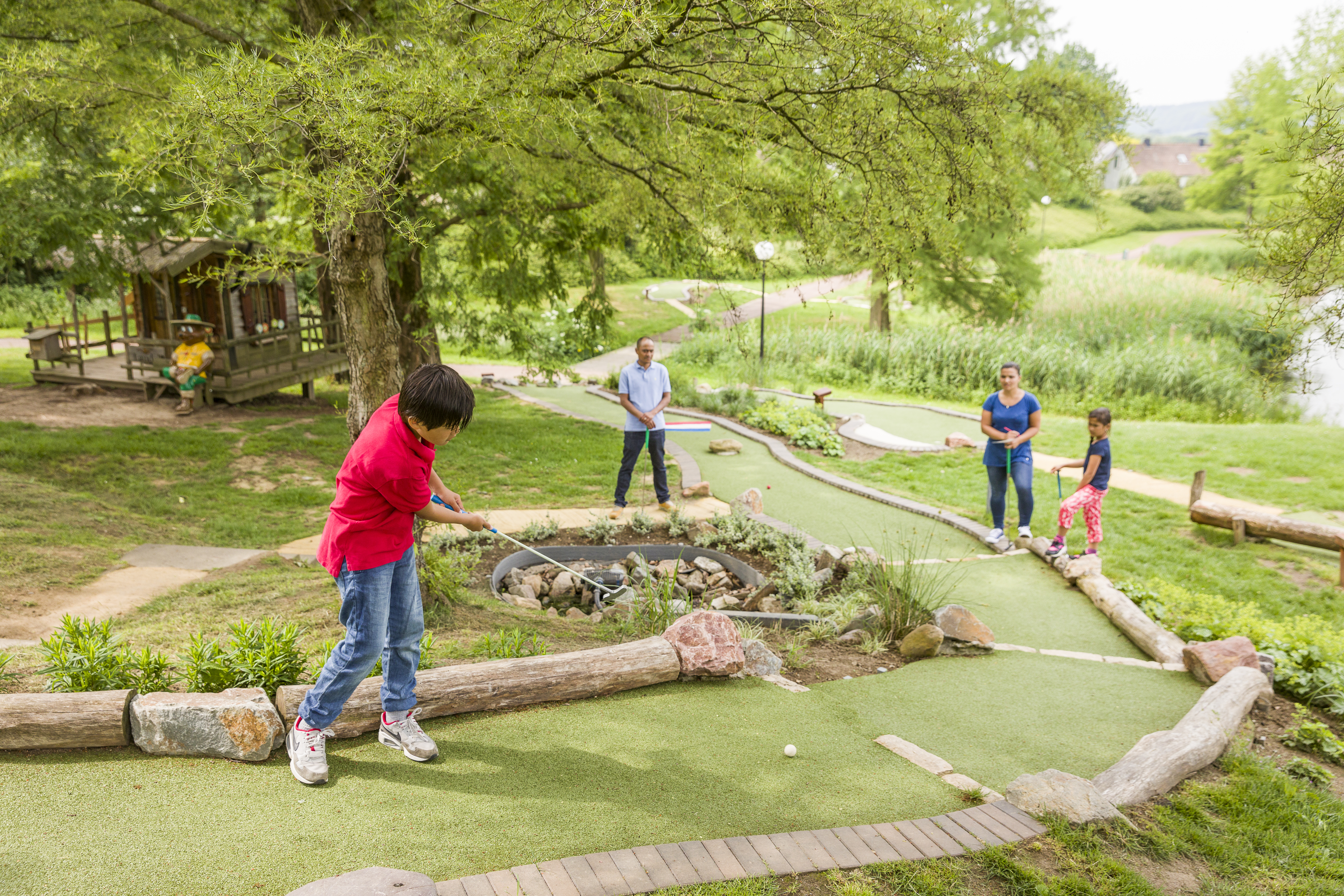 Een gezin speelt midgetgolf op de avontuurlijke midgetgolfbaan, die is aangelegd in een natuurlijke, groene omgeving op Landal Hoog Vaals.