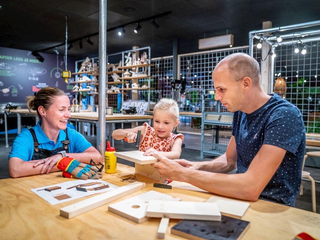 Een gezin is samen een houten vogelhuisje aan het bouwen aan een werktafel in de knutselwerkplaats van Landal Hoog Vaals.