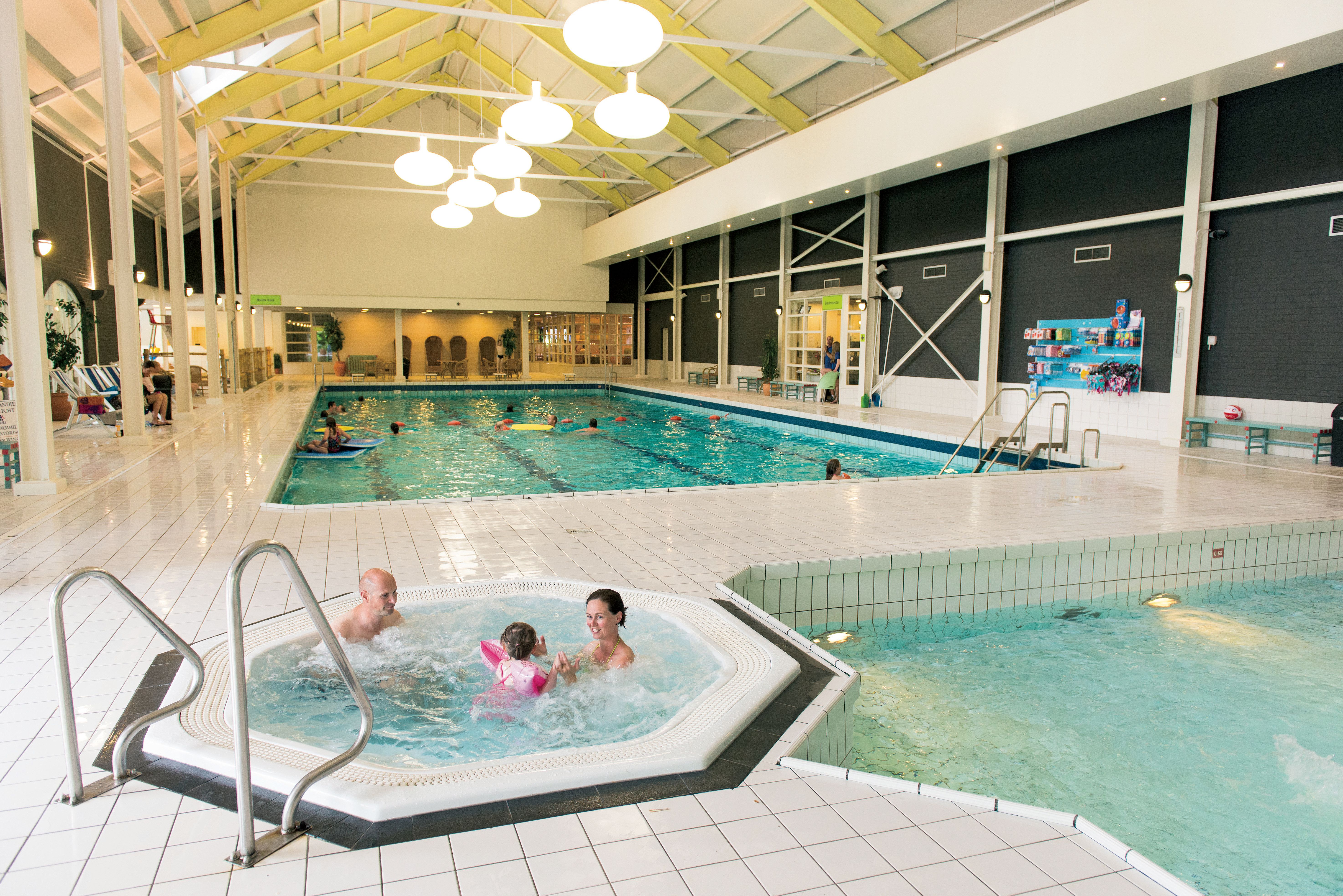 Een gezin met een jong kind ontspant in de warme whirlpool naast het grote overdekte zwembad van Landal Hoog Vaals.