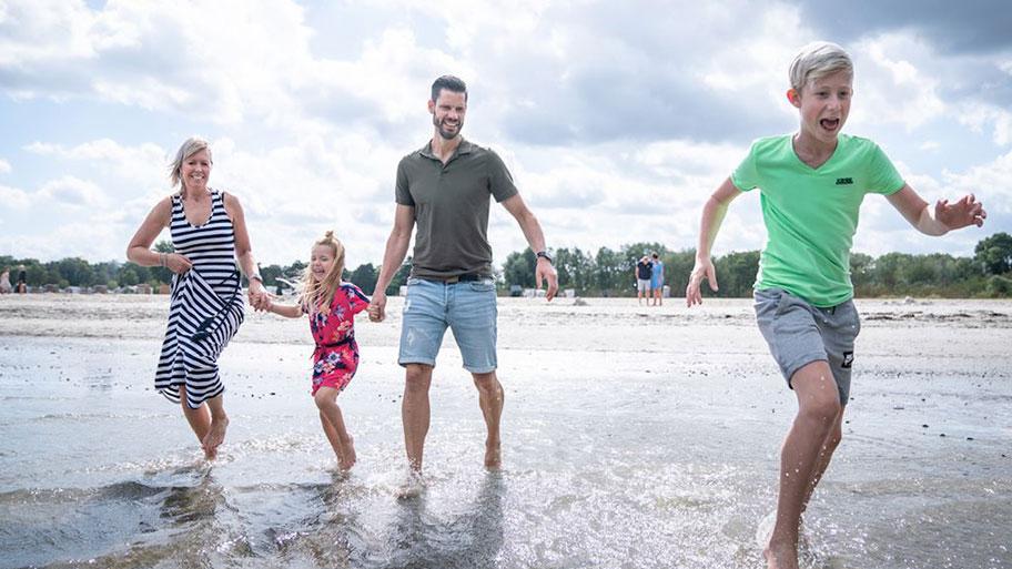 Lachende familie met kinderen spettert en speelt in het ondiepe water bij Landal Marissa, genietend van strand en meer.