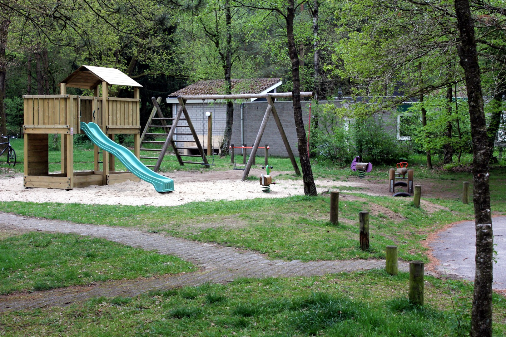 Speeltuin met een glijbaan, schommels en een wipkip, omringd door groen gras en bomen op Parc de Berkenhorst.