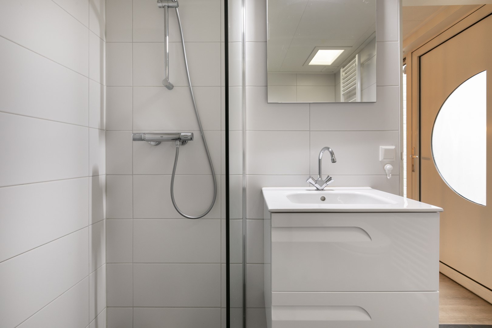 De moderne, witte badkamer in een bungalow op Parc de Berkenhorst, met een inloopdouche en wastafel.