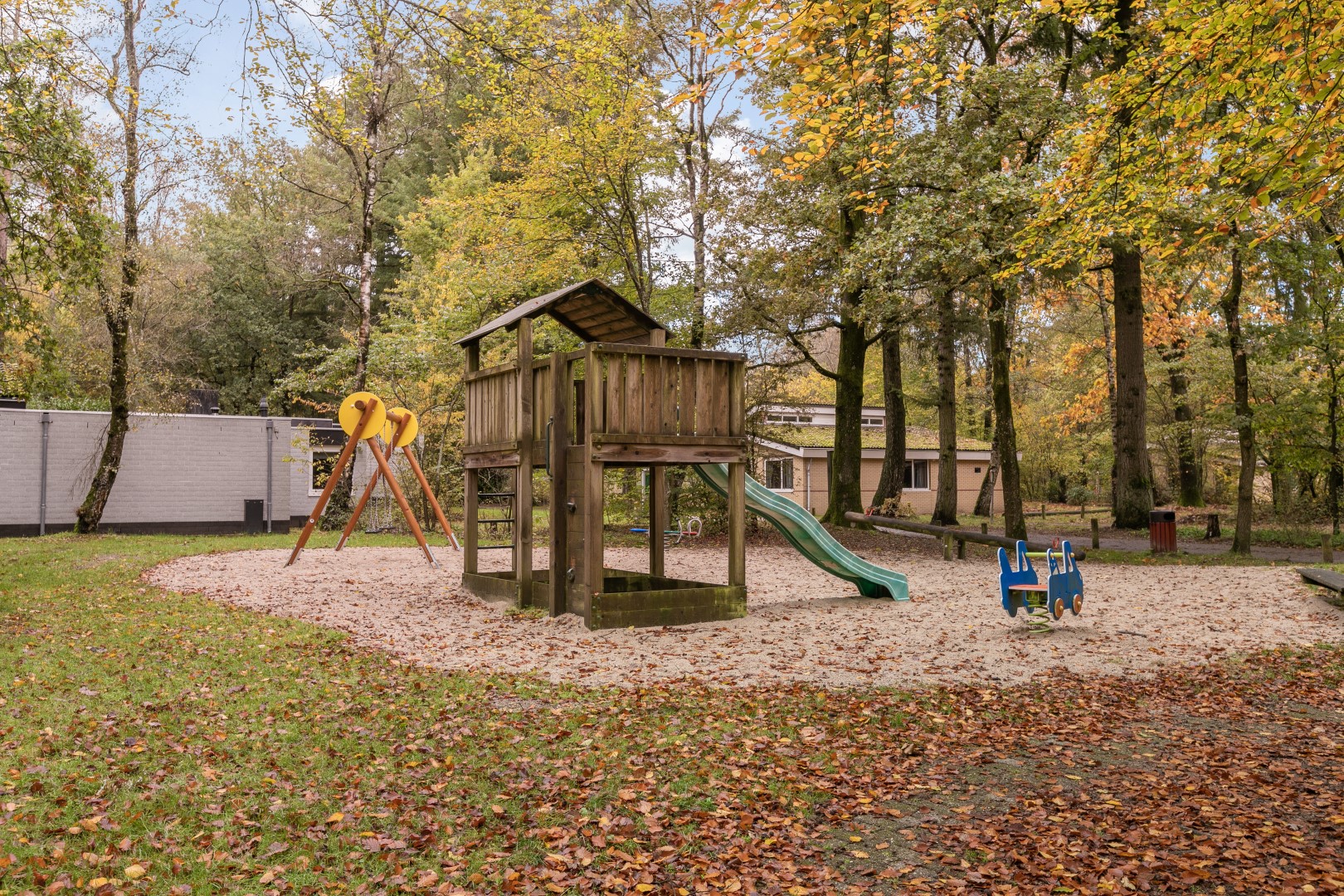 Houten speeltuin met glijbaan en schommels, omringd door herfstbladeren in het bos op Parc de Berkenhorst.
