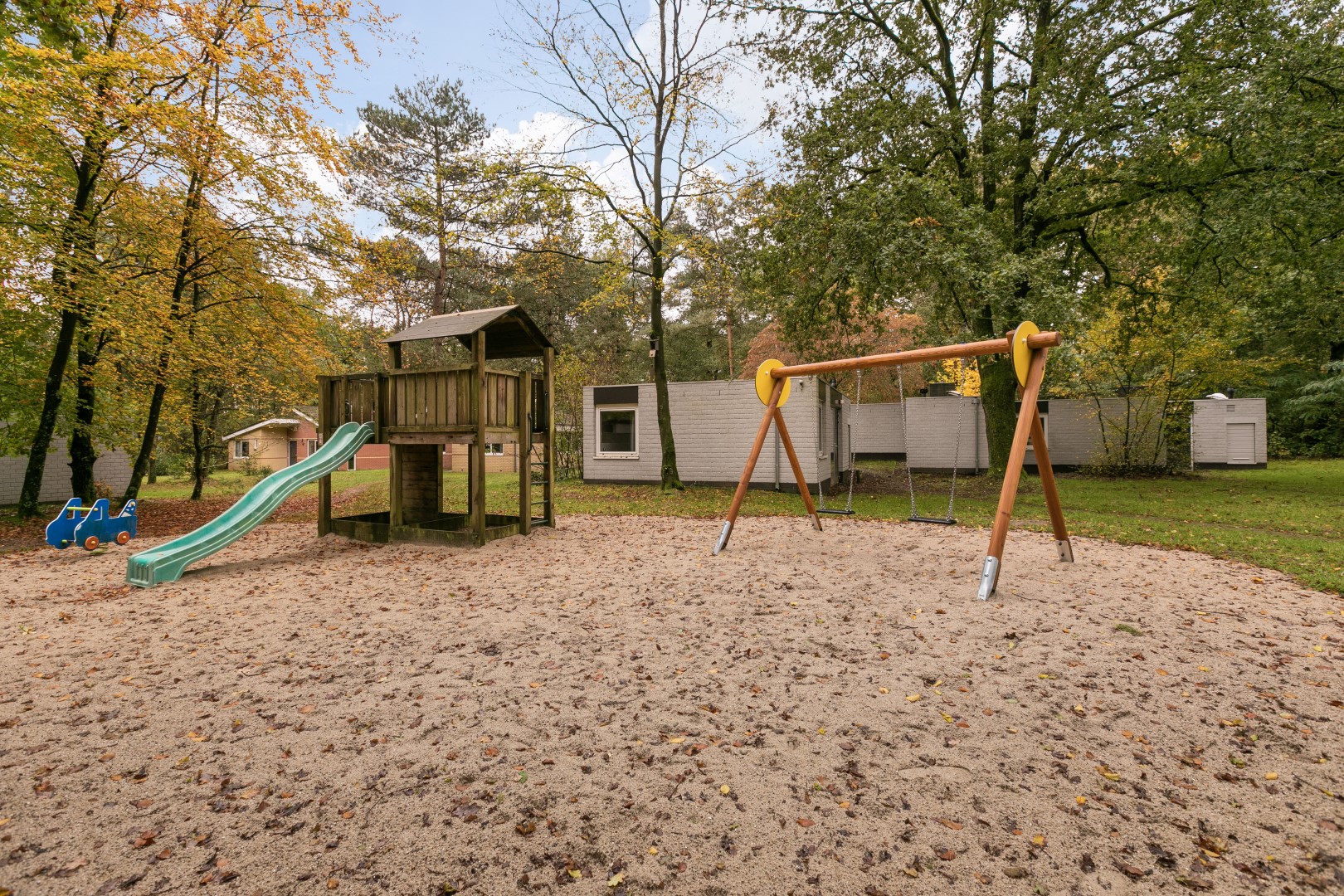 Een speeltuin met een grote zandbak, een glijbaan en schommels, gelegen tussen de bomen op Parc de Berkenhorst.