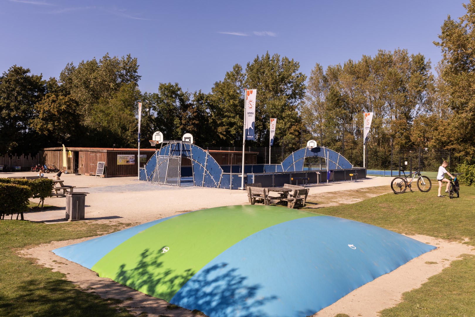 Een grote, kleurrijke airtrampoline voor kinderen om op te springen bij Vakantiepark Port Greve, met een sportkooi in de achtergrond.