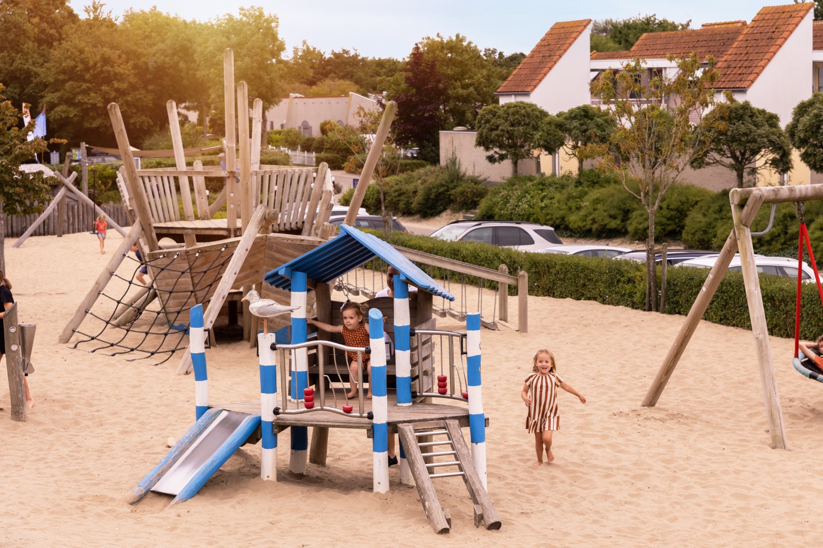 Twee jonge kinderen spelen in een grote zandspeeltuin met een houten klimtoestel en glijbaan op Vakantiepark Port Greve.